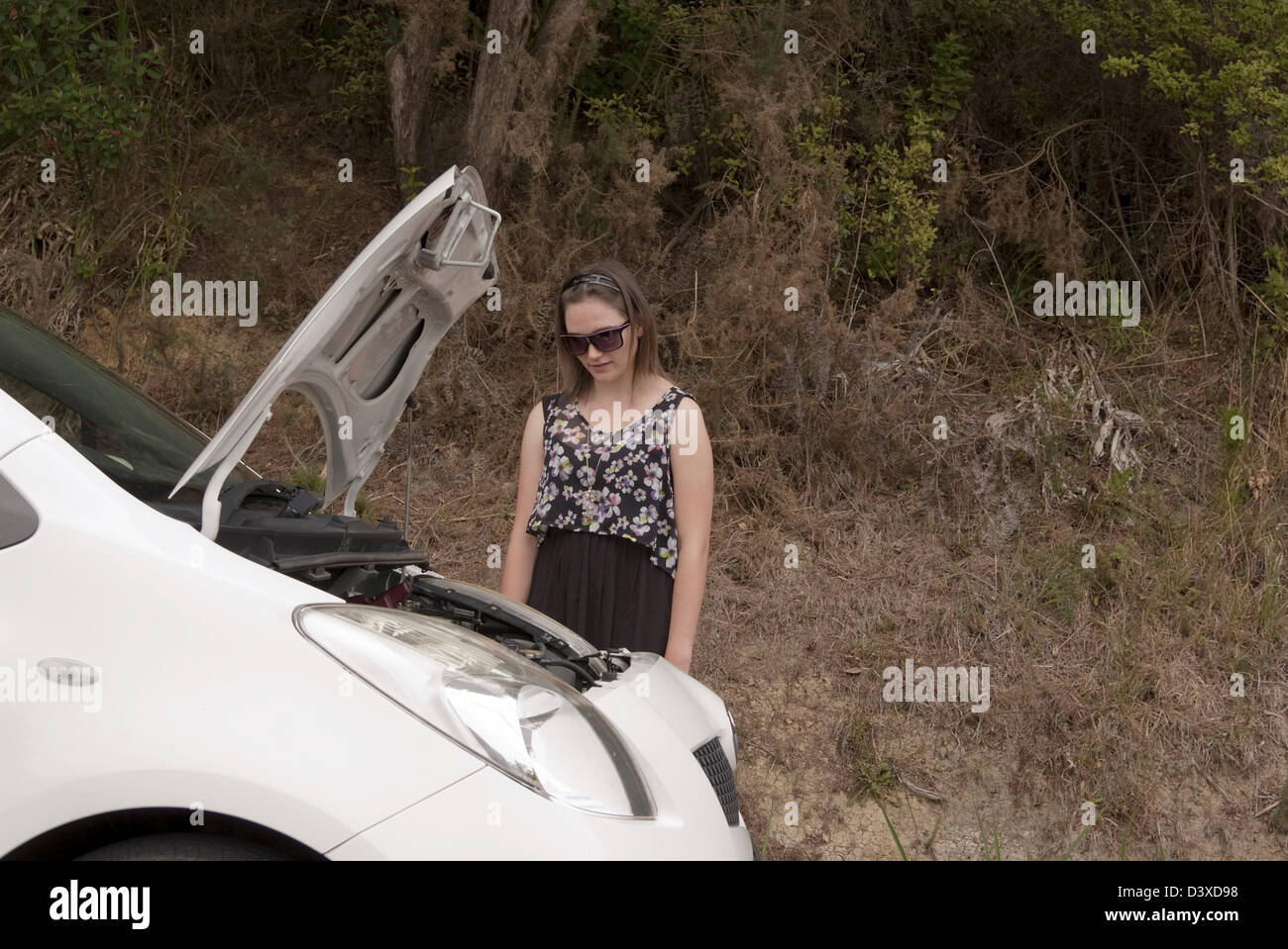 A young woman looks concerned at her car with the bonnet open. Stock Photo