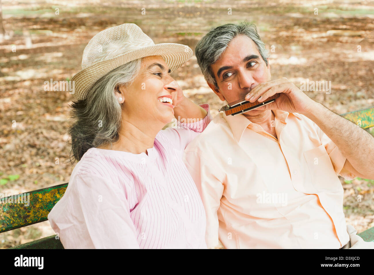 Man playing a harmonica with his wife sitting beside him and smiling, Lodi Gardens, New Delhi, India Stock Photo