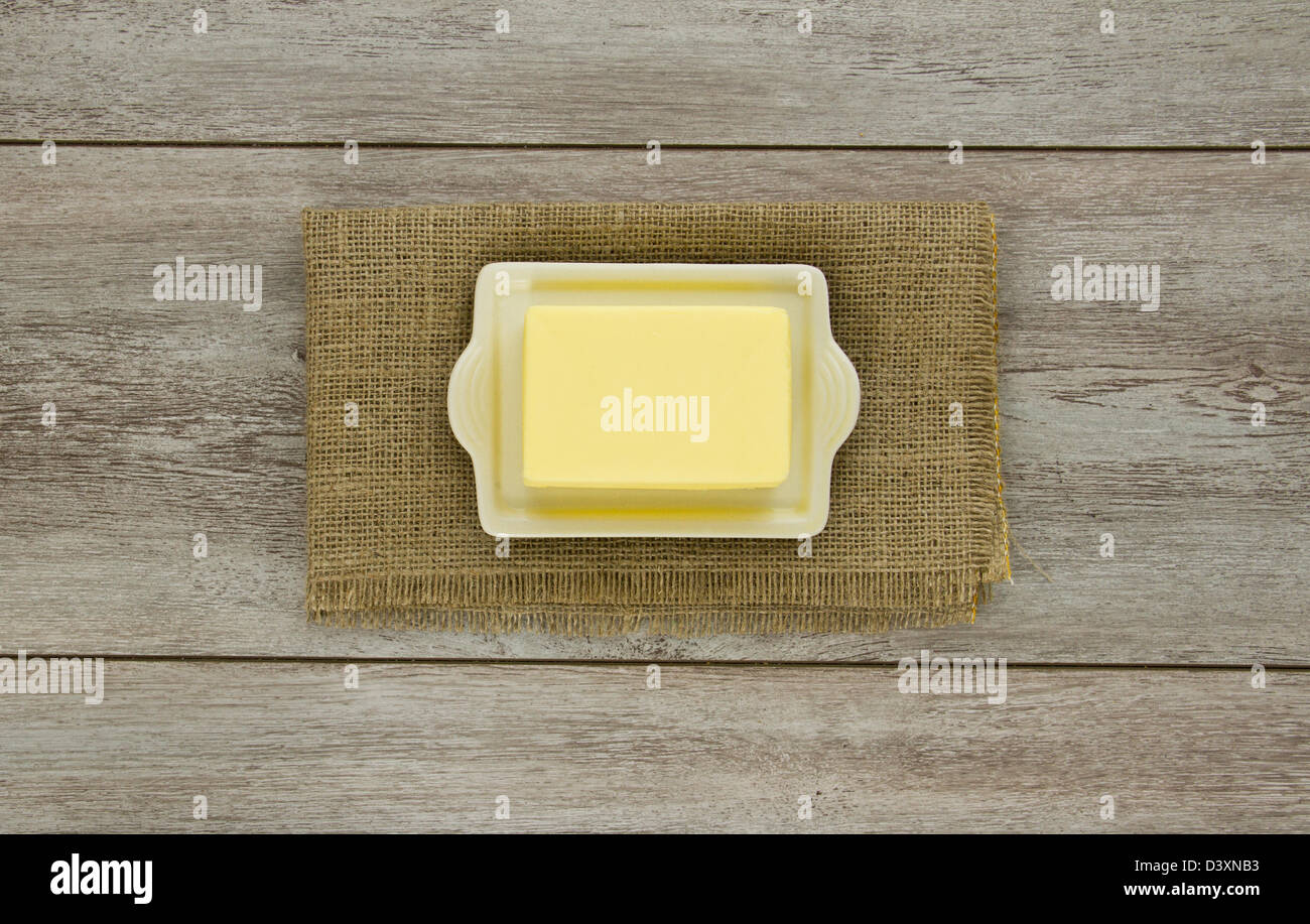 A creamy block of yellow butter on a cream ceramic butter dish on burlap. On weathered boards. Stock Photo