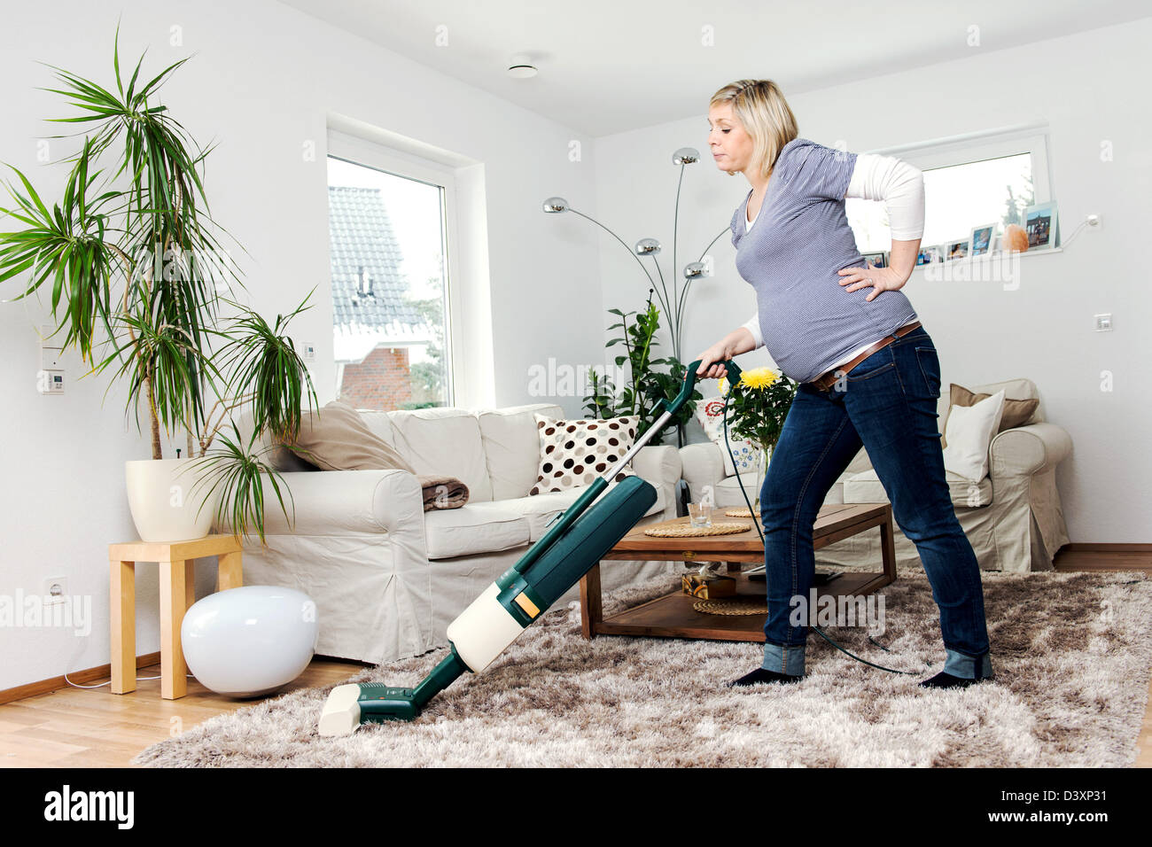 A pregnant woman sucks in living room with a vacuum cleaner a carpet