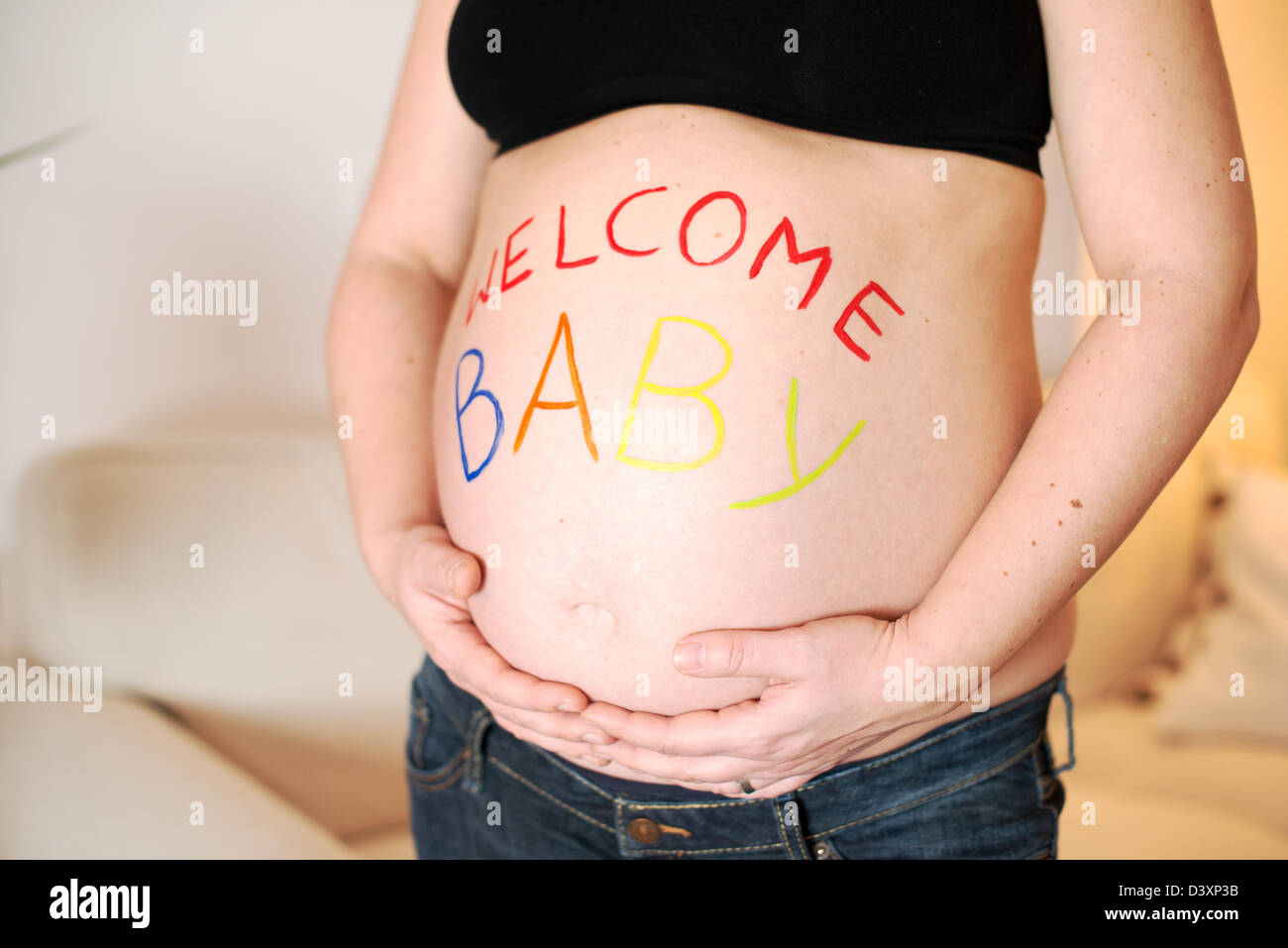 'Welcome Baby' is painted in colorful letters on the baby belly of a pregnant woman. Stock Photo