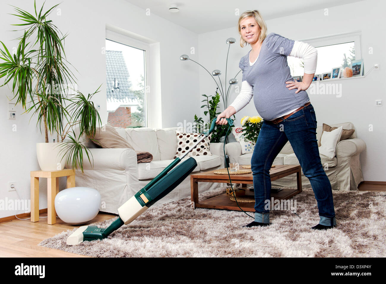 A pregnant woman sucks in living room with a vacuum cleaner a carpet