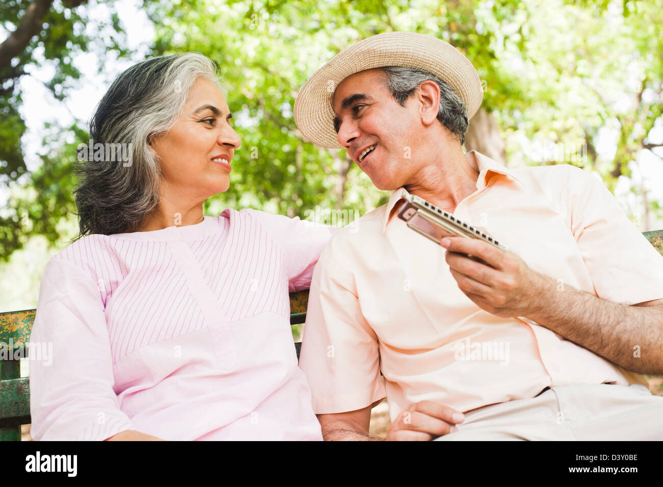 Man playing a harmonica with his wife sitting beside him and smiling, Lodi Gardens, New Delhi, India Stock Photo