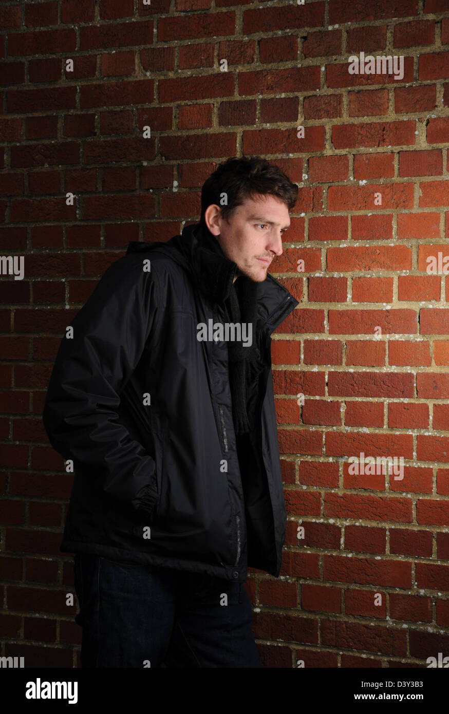 Generic shot of shady character male against red brick wall posed by model wearing black North Face jacket Stock Photo