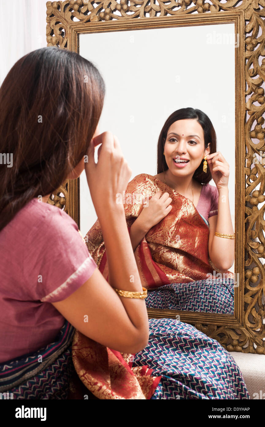 Reflection of a woman in mirror trying a sari and earring on herself Stock Photo