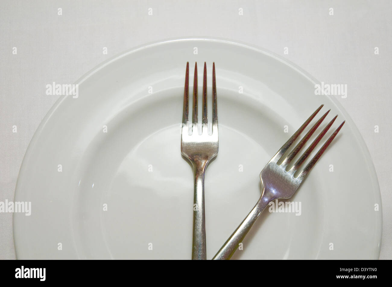 Two forks striking two o'clock on a plate. Stock Photo