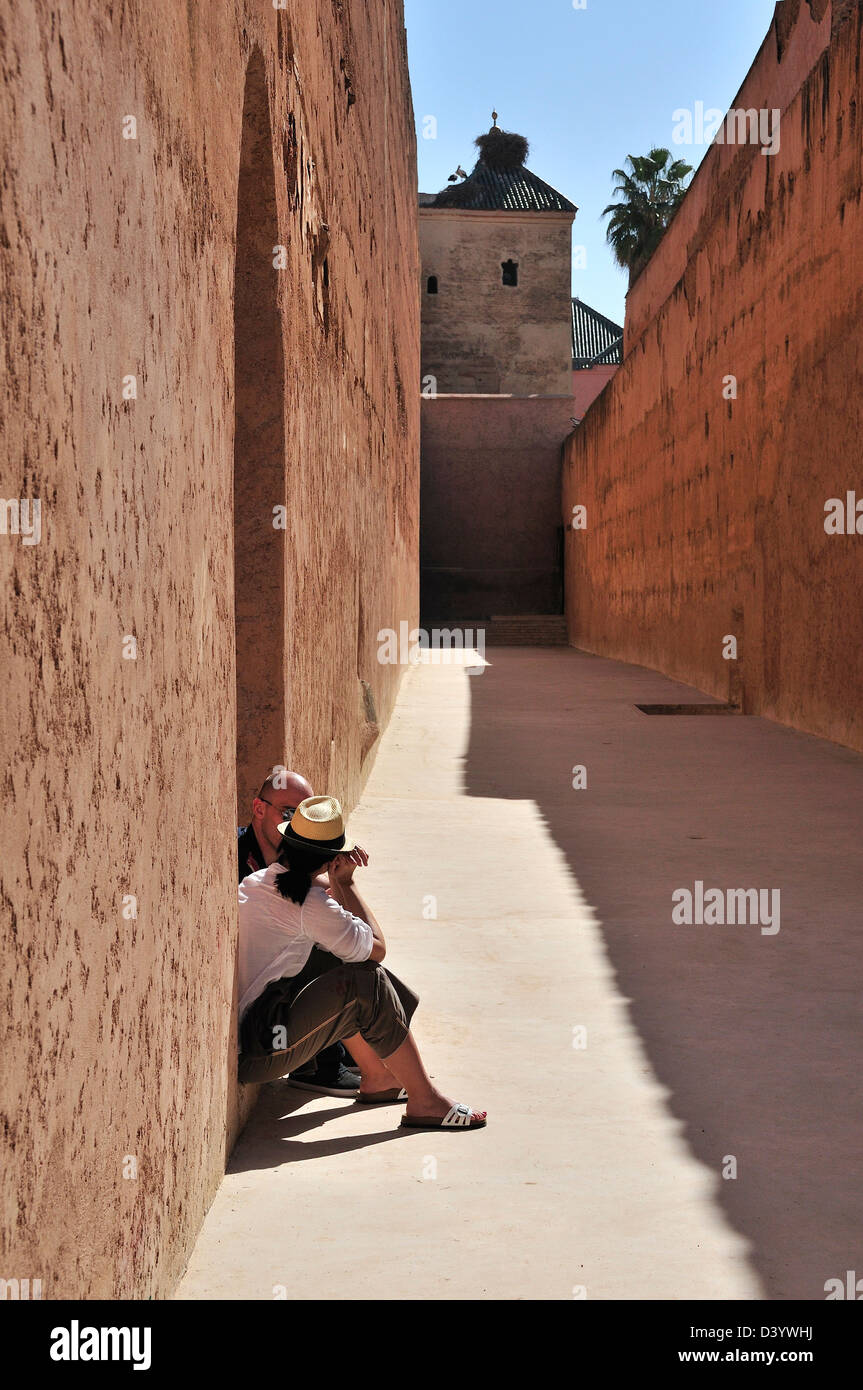 Couple couple sitting on step between two ancient pink hued high walls at the El Badii Palace, Marrakech, Morocco Stock Photo