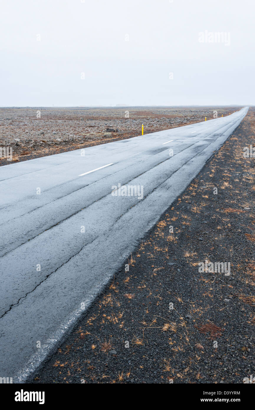 A straight empty wet open road in Iceland on a dull day taken at a low and wide angle. Shows converging perspective to horizon Stock Photo