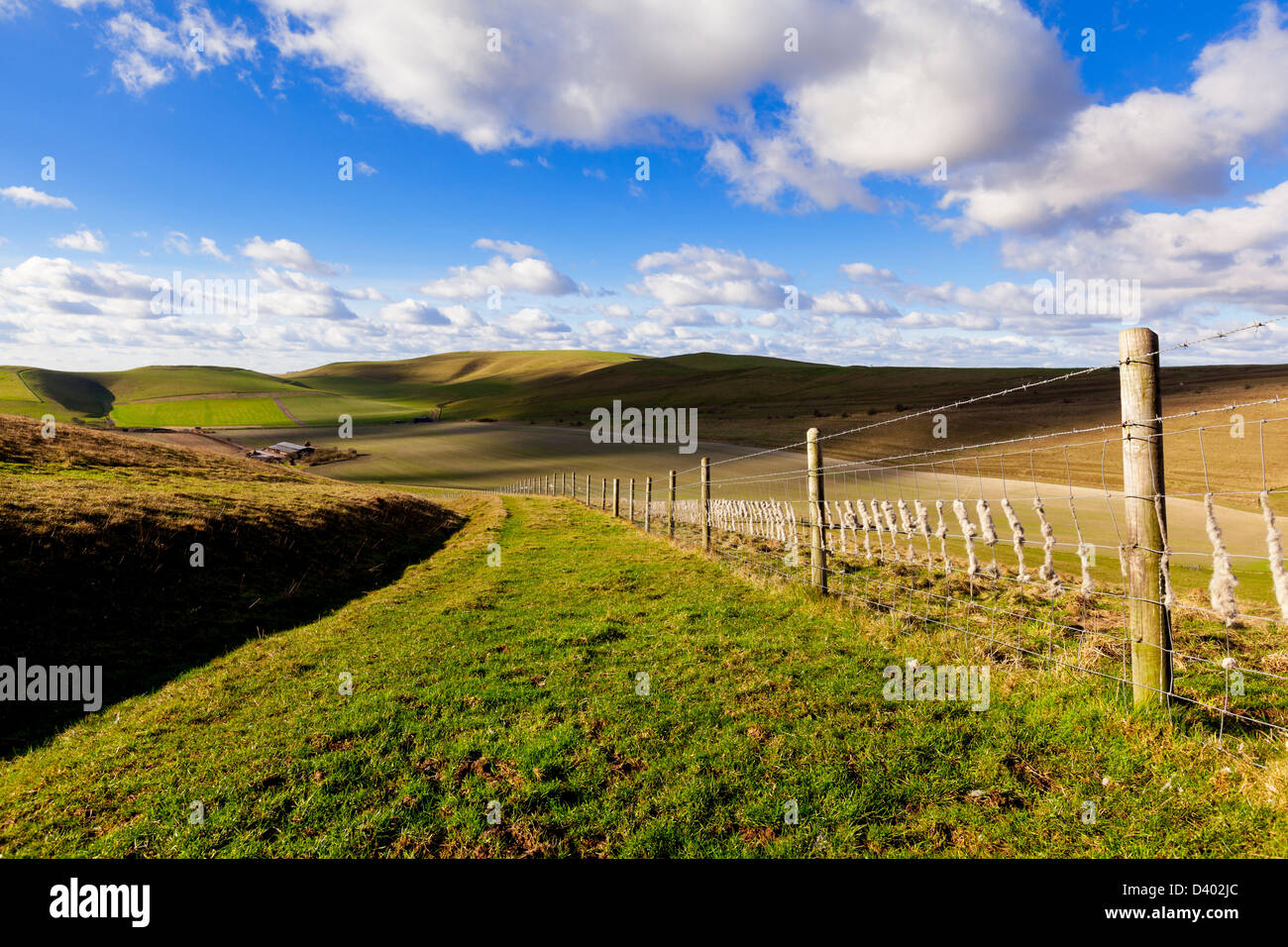 A wide grassy track and a barbed wire fence set amongst rolling green hills on the Pewsey Downs in Wiltshire, UK Stock Photo