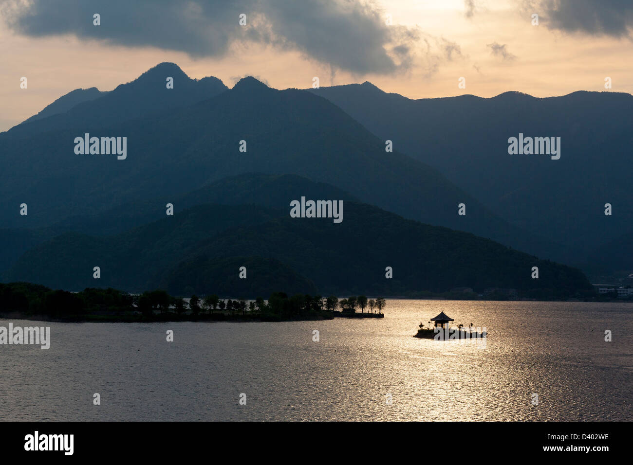 Sunset silhouette of the island shrine on lake Kawaguchi with mountains in the background. Stock Photo