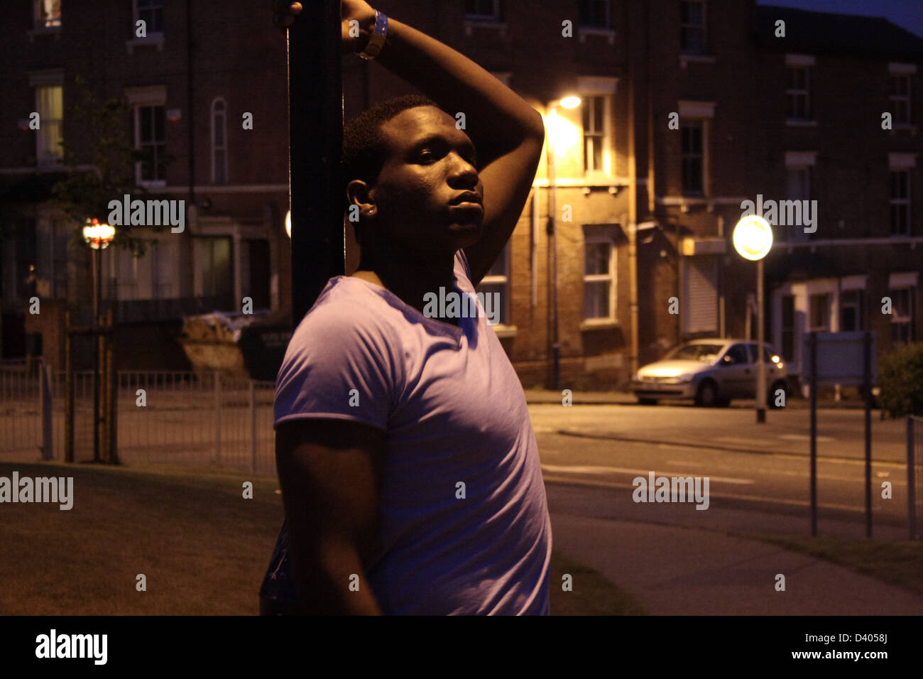 Black man leaning onto a street lamp at night, with his left arm raised. Stock Photo
