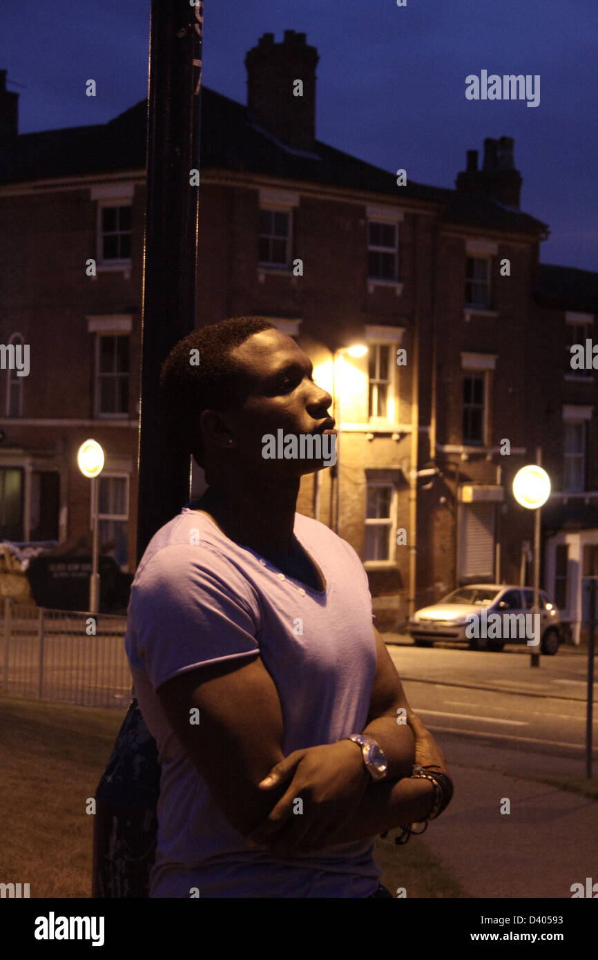 Black man leaning onto a street lamp at night. Stock Photo