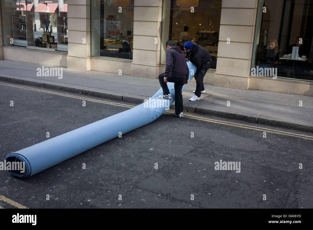 A team of Asian men are about to carry a roll of industrial carpet in a side street and destined