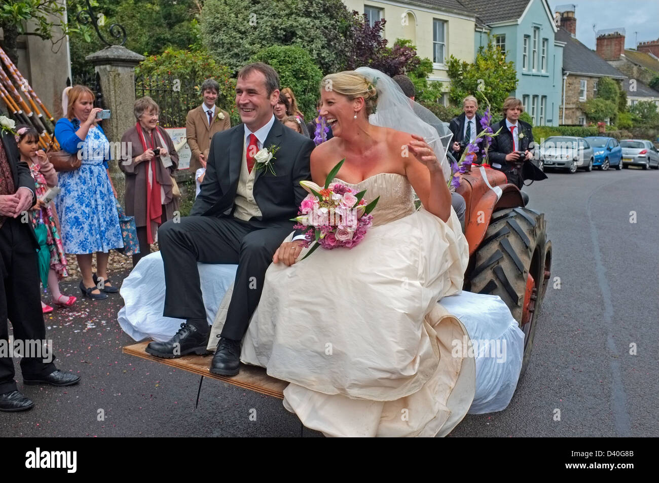 A newly married couple leave the church on a tractor. Stock Photo
