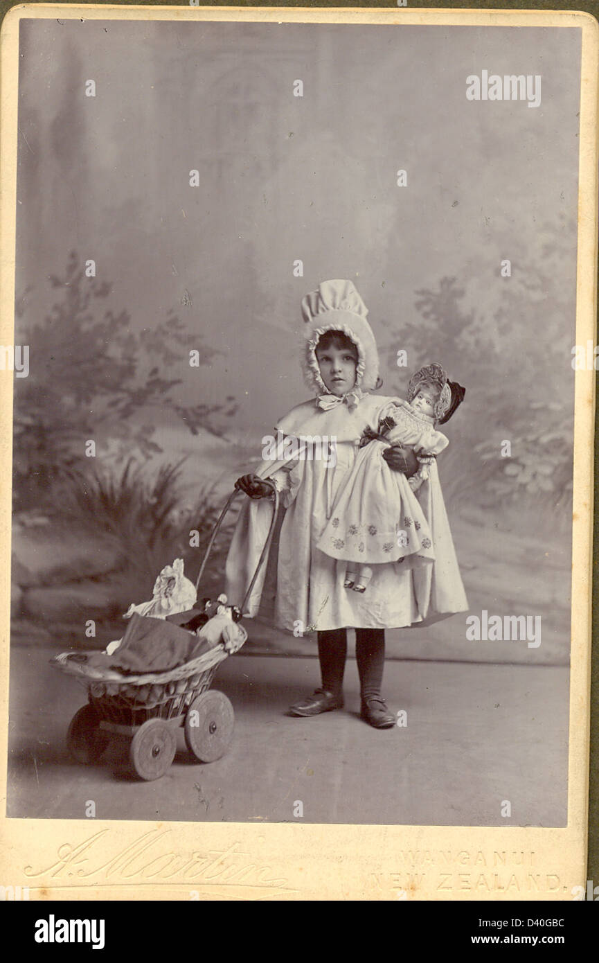 Portrait cabinet photograph of  a very solemn small girl, Joyce Carr Shields 1895 with her  doll's pram and dolls Stock Photo