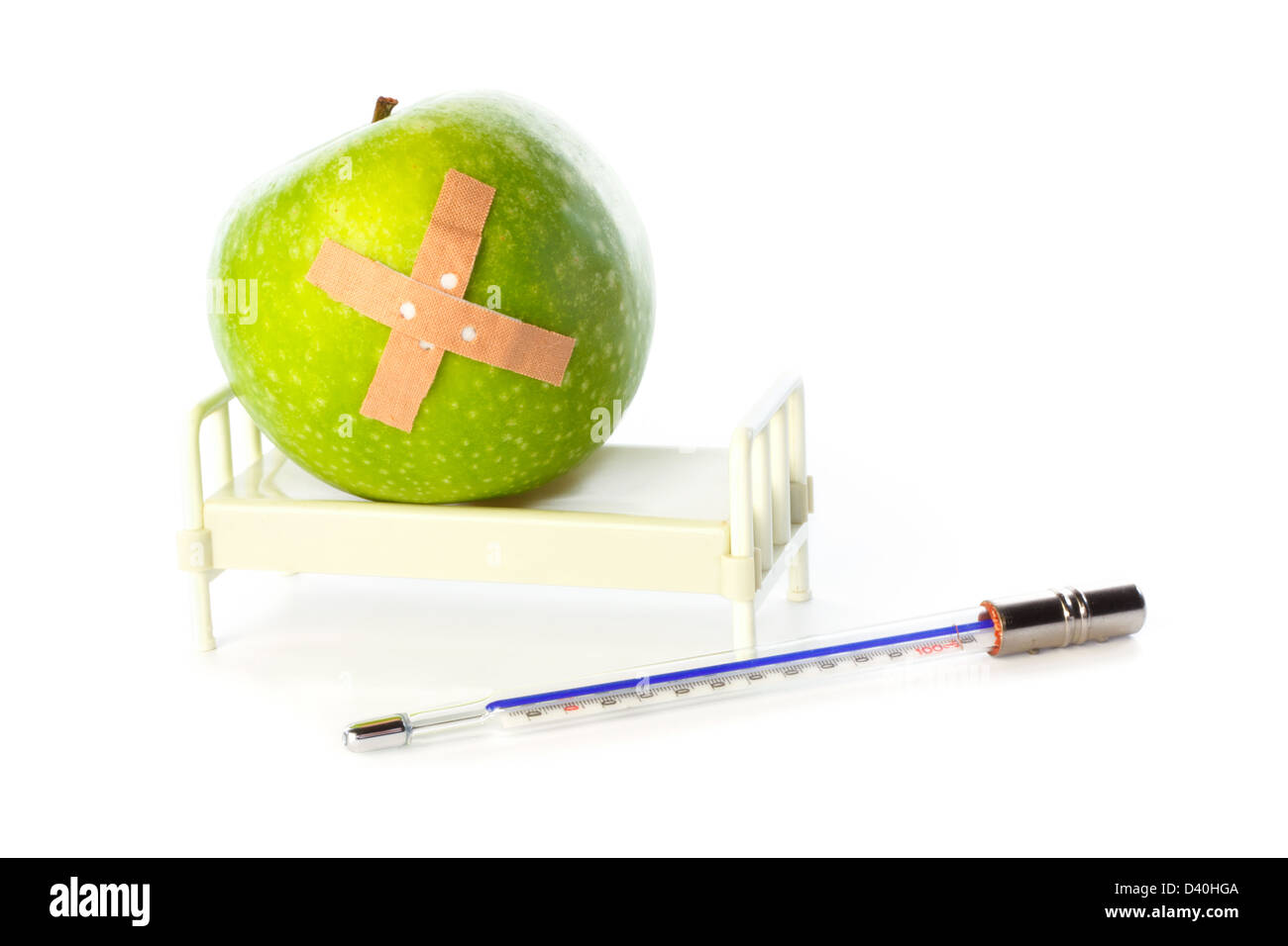 Apple with bandage in hospital bed and thermometer in front Stock Photo