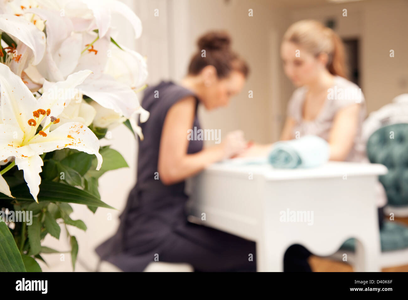 A young woman having her nails painted in a beauty salon. The subjects are in the background with a vase of flowers to the left Stock Photo