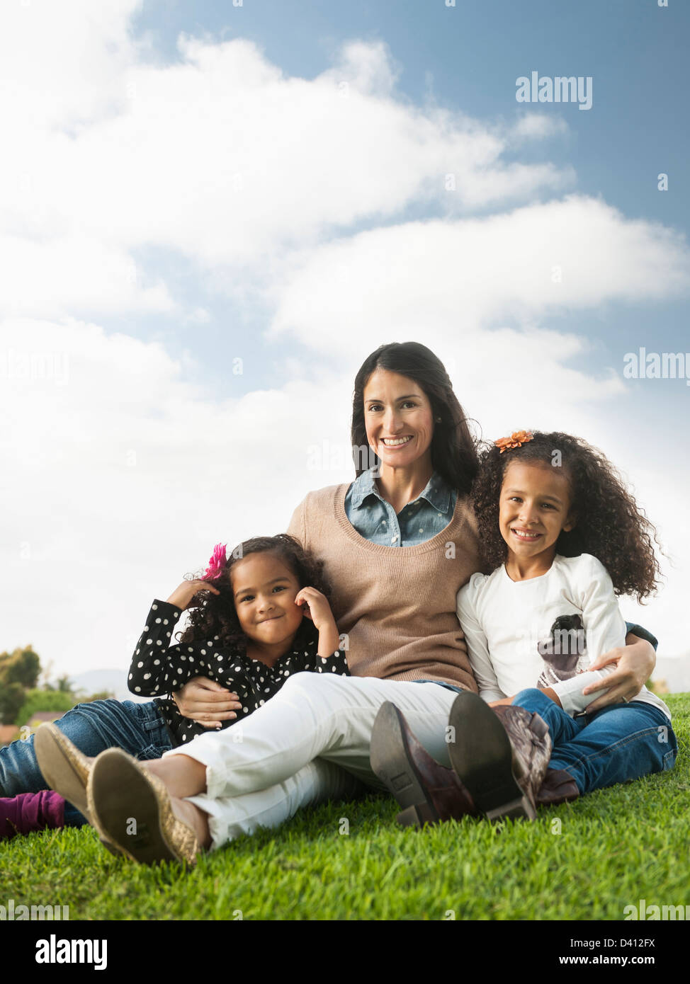 Mother and daughters sitting in grass Stock Photo