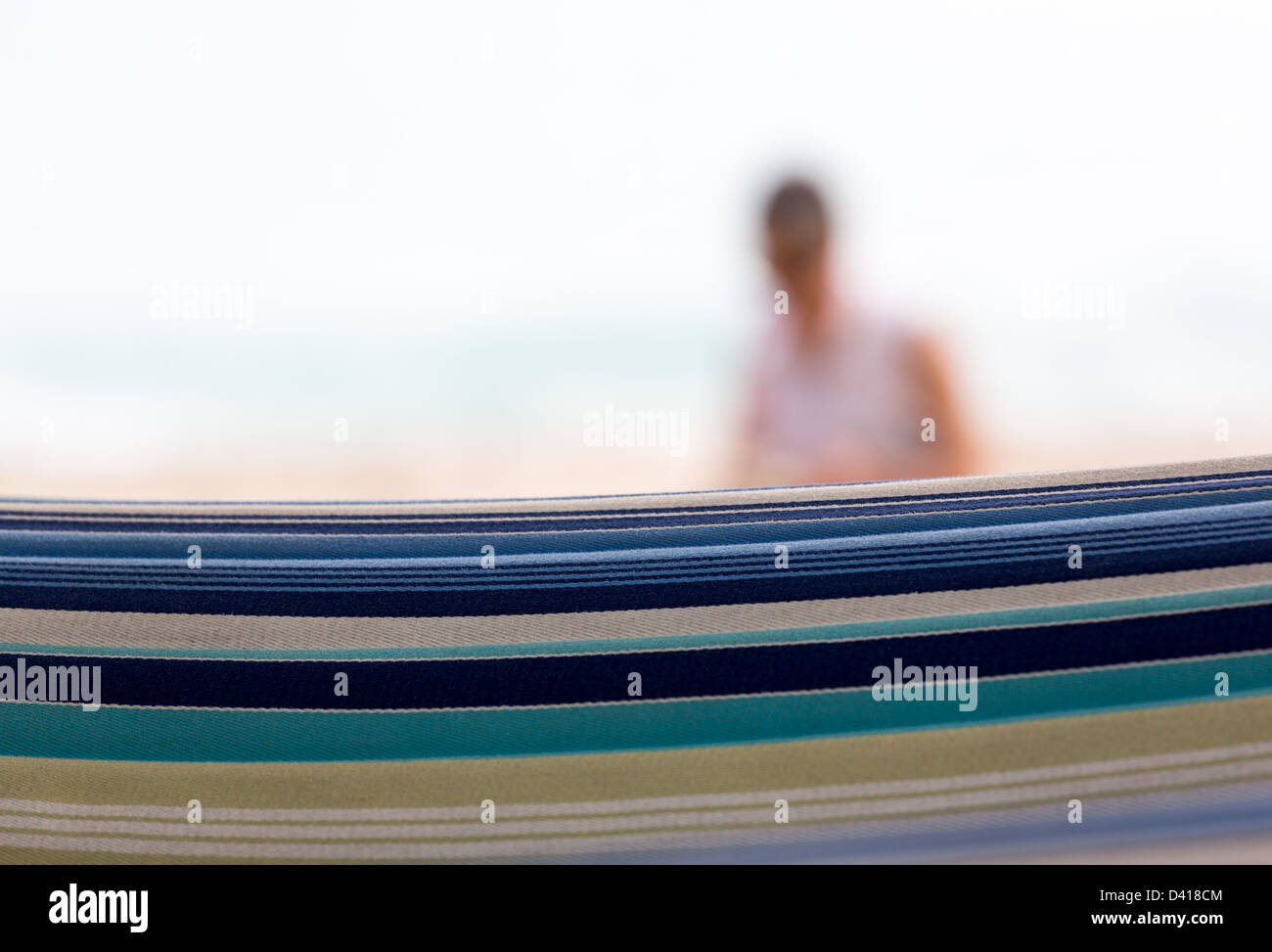 Close focus on the fabric of hammock with a blurred lady on beach in distance Stock Photo