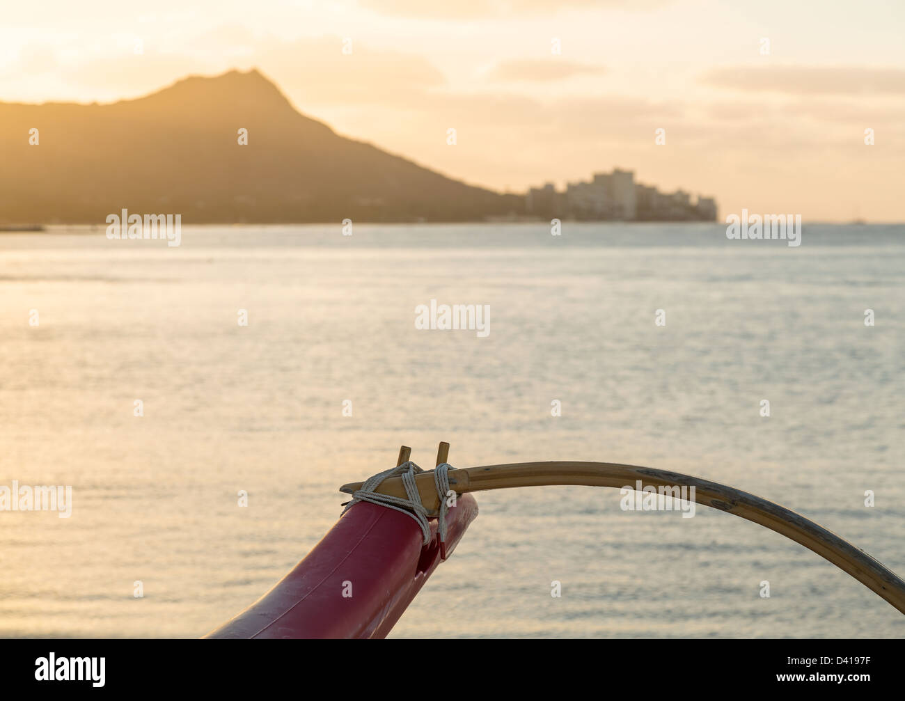 Early morning sunrise at dawn illuminates outrigger of traditional Hawaiian canoe by Diamond Head and Waikiki Beach area of Oahu in Hawaii Stock Photo
