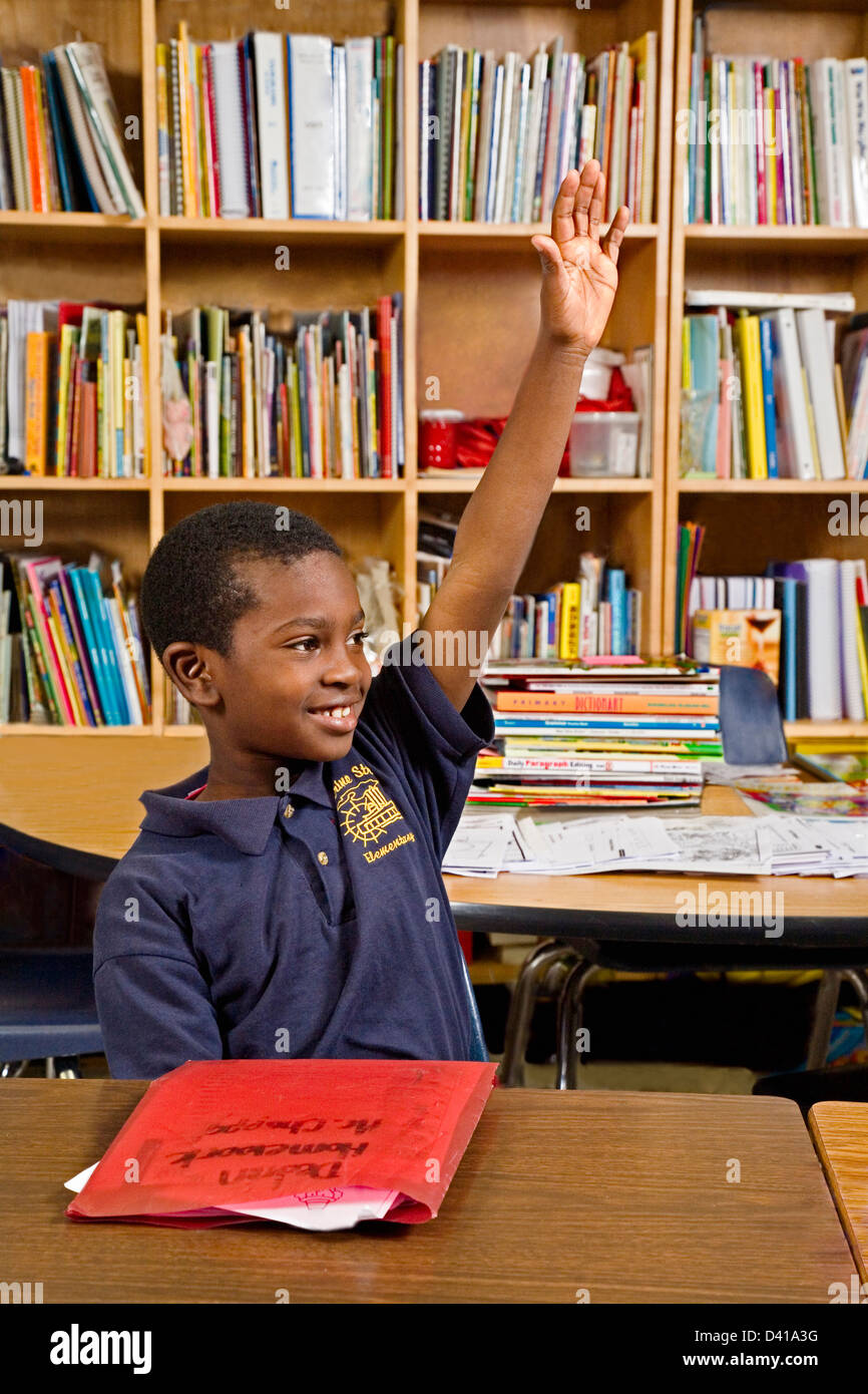 Black second grade male student sits at desk and raises his hand in