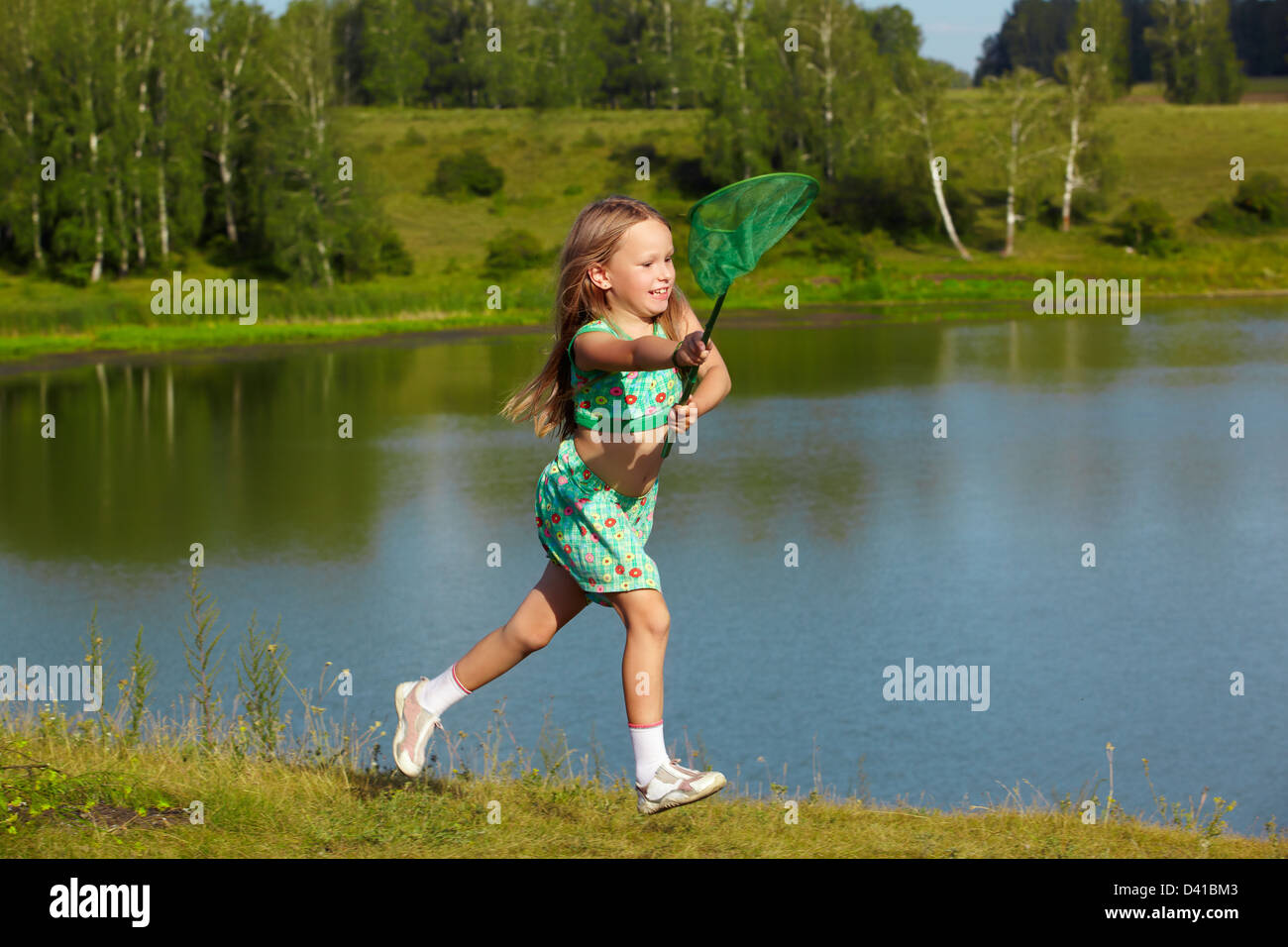 outdoor portrait of little girl running with butterfly net along the bank of the pond Stock Photo