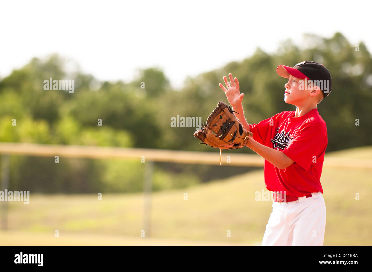Young baseball player in red jersey about to catch the pop fly Stock