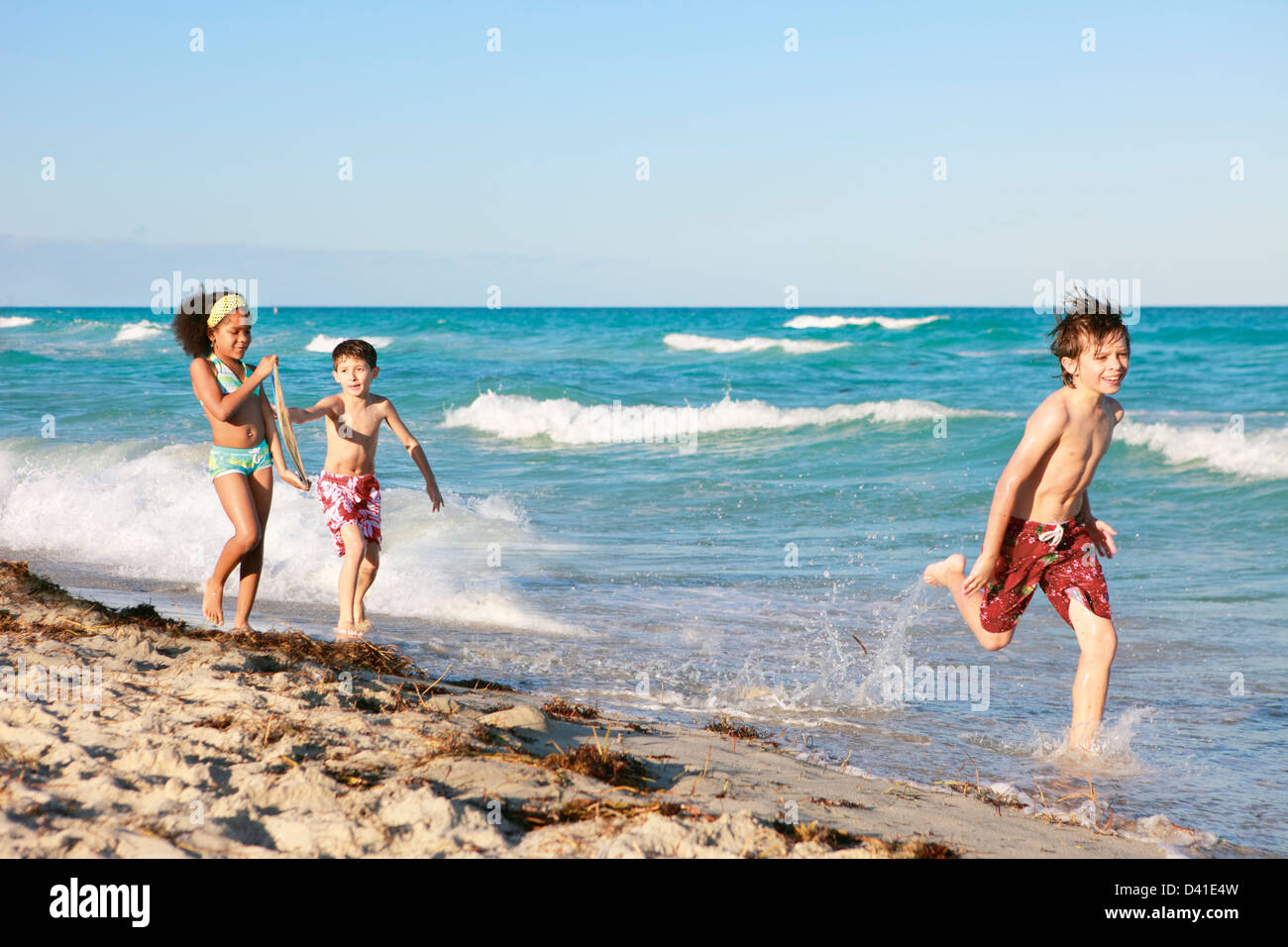 Three school-aged kids having fun playing on the beach Stock Photo