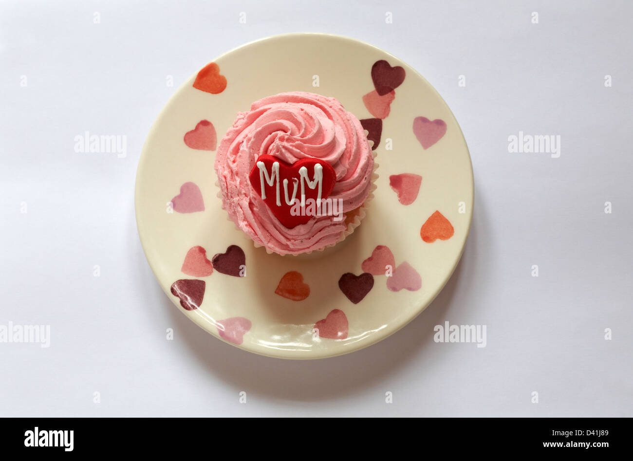 strawberry cupcake with the word mum iced on red heart for Mothering Sunday, Mothers Day set on plate with hearts on isolated on white background Stock Photo