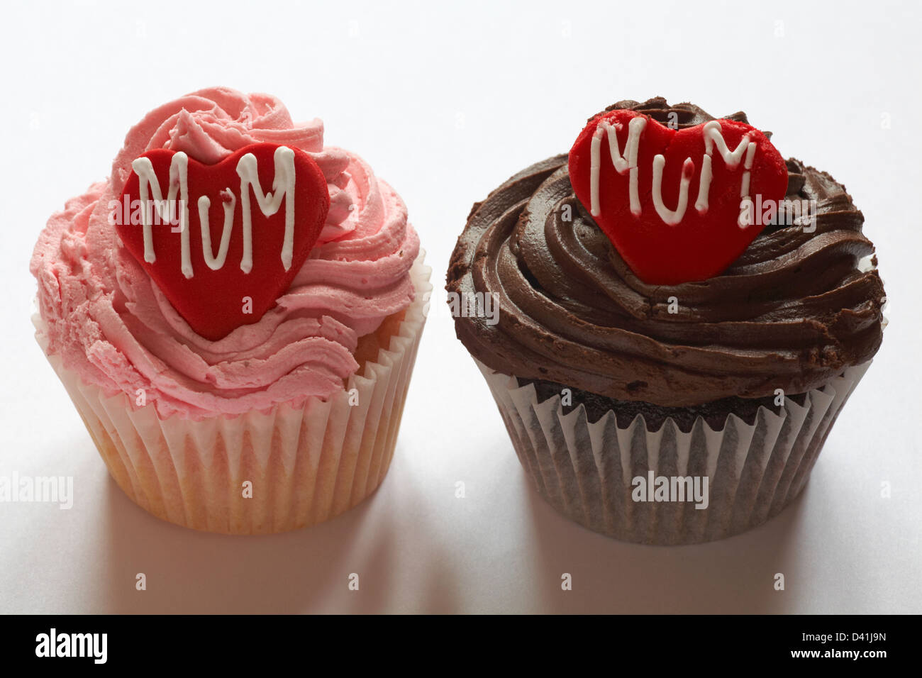 strawberry cupcake and chocolate cupcake with the word mum iced on red heart for Mothering Sunday, Mothers Day isolated on white background Stock Photo