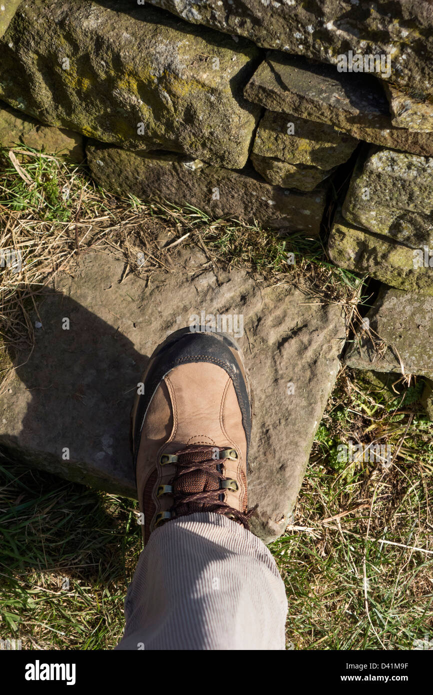 Close up of walking boot on the step of a stone stile on a public footpath, UK Stock Photo
