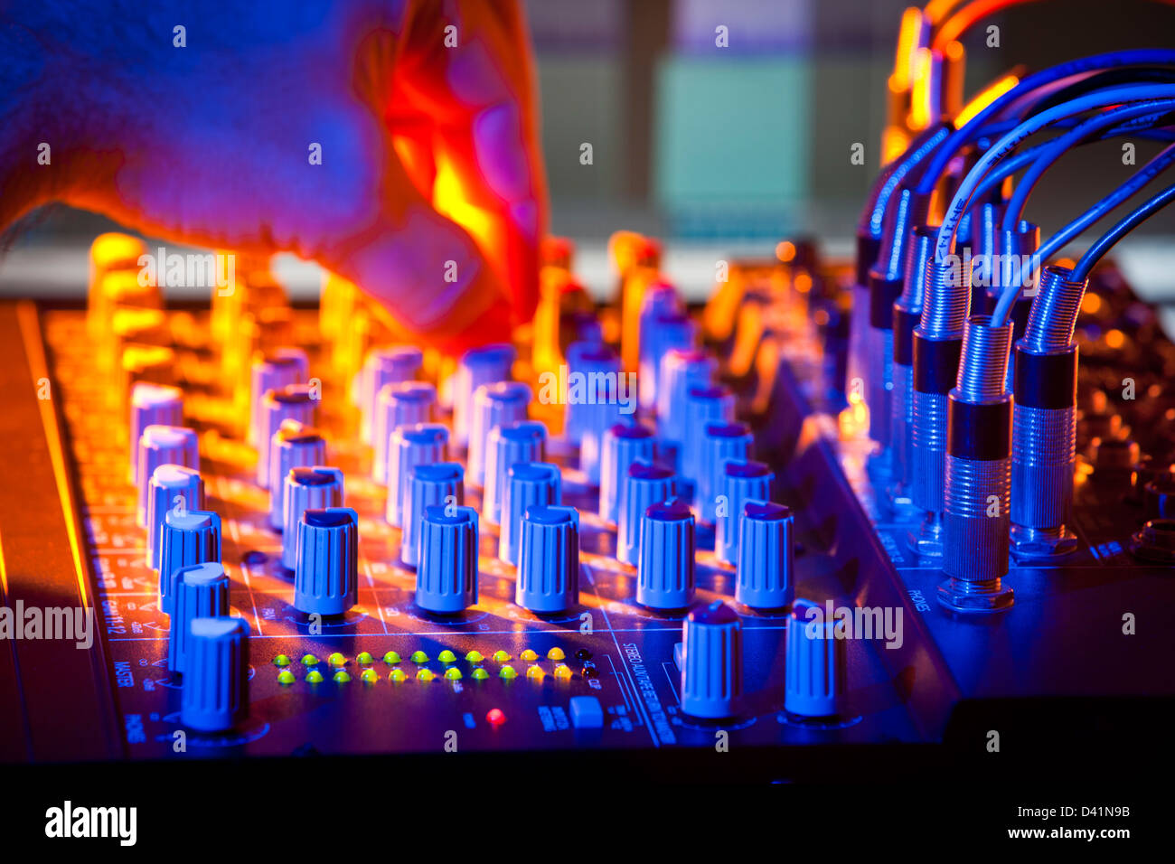 Close-up of audio mixing desk. Motion blurred hand on distant controls. Selective focus on foreground LEDs. Stock Photo
