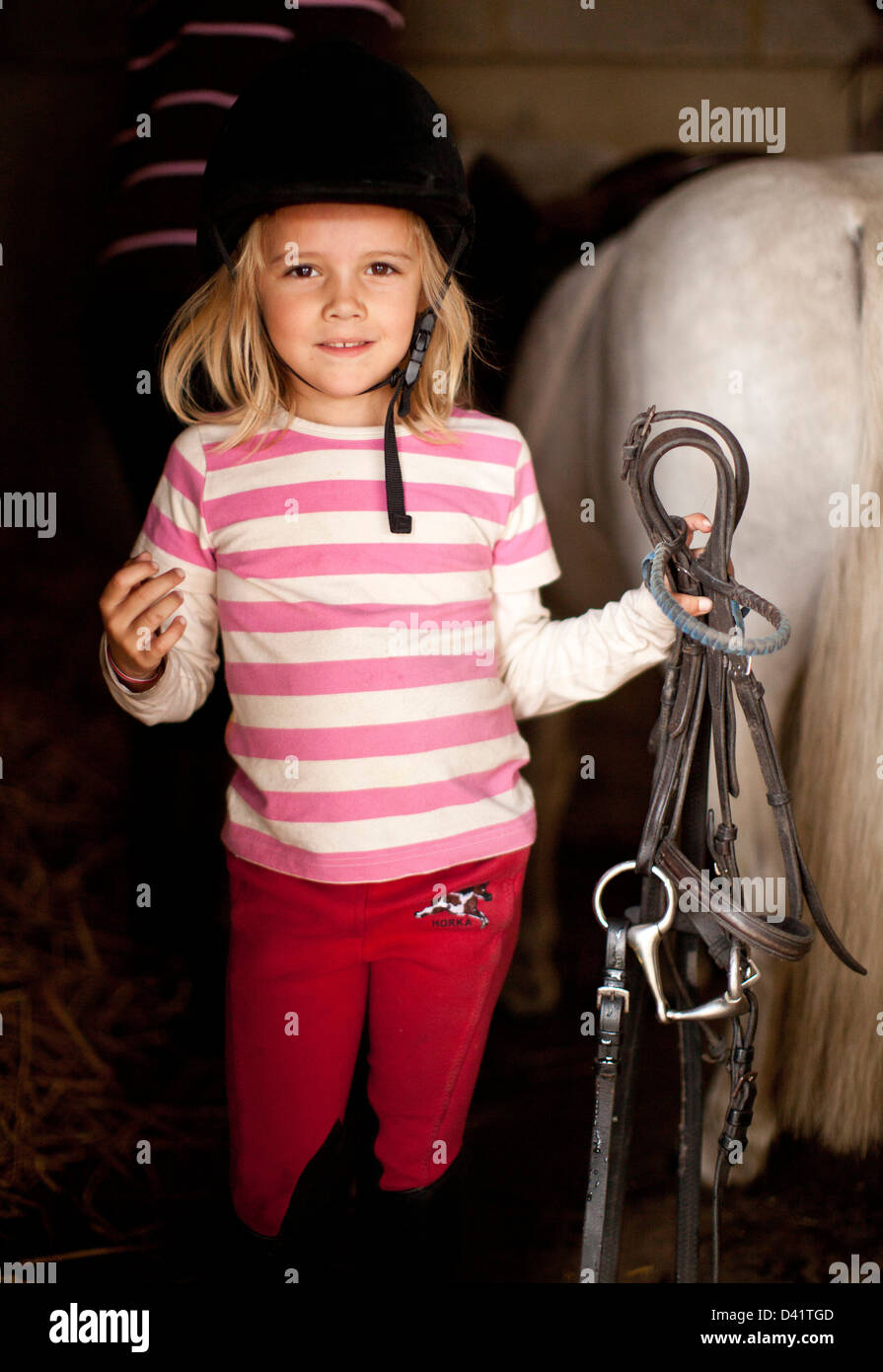 Young girl holding bridle for pony in stables, London, UK Stock Photo