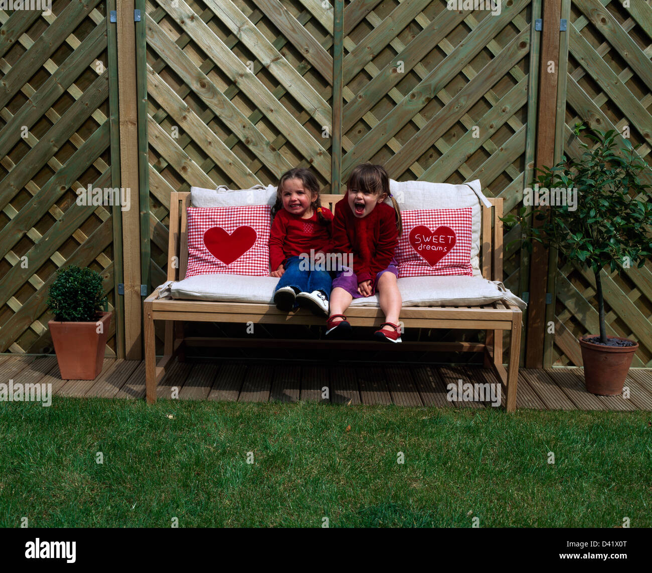 Two small girls wearing red jerseys sitting on garden bench Stock Photo