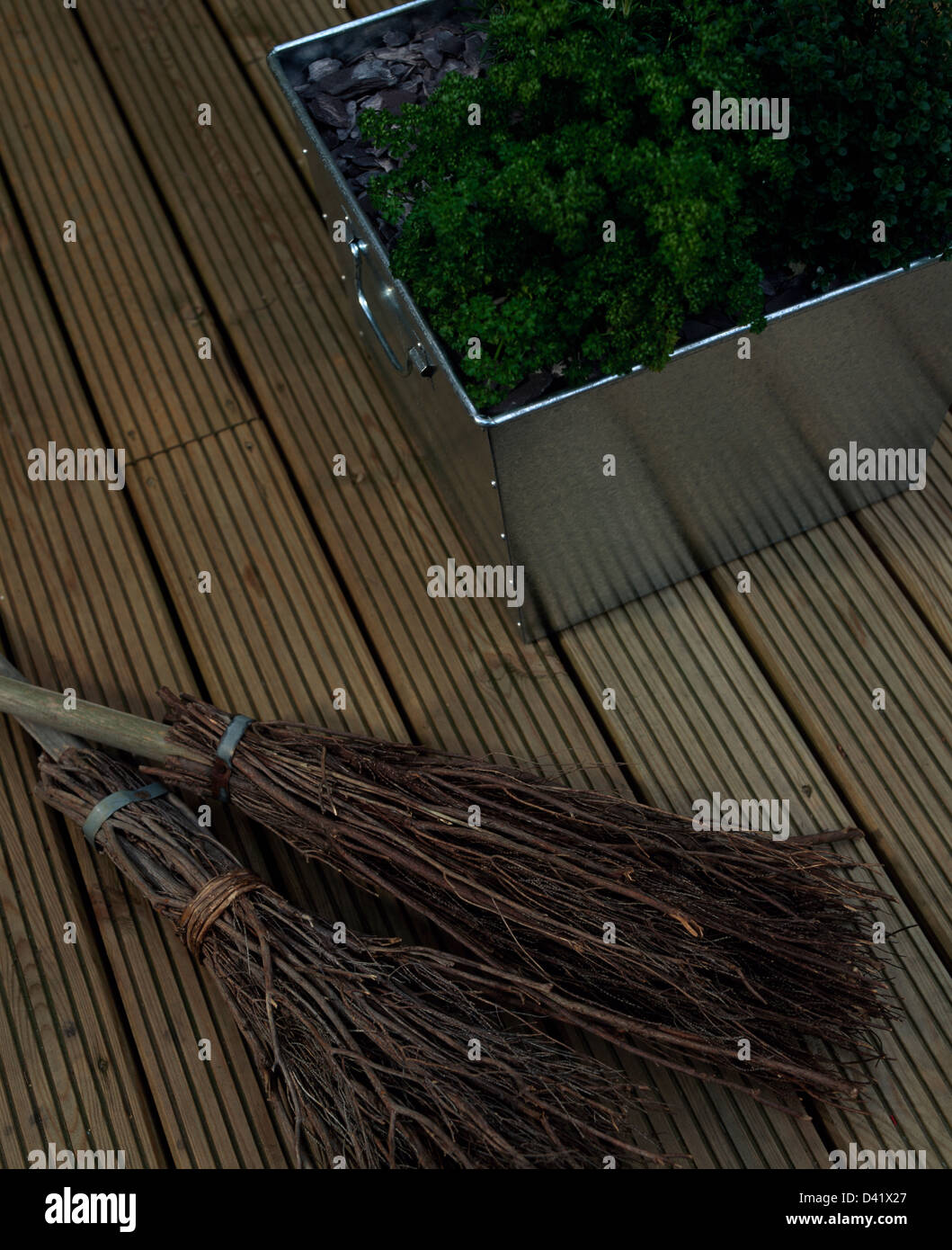 Close-up of two besom brooms on wooden decking with herbs growing in galvanized steel planter Stock Photo