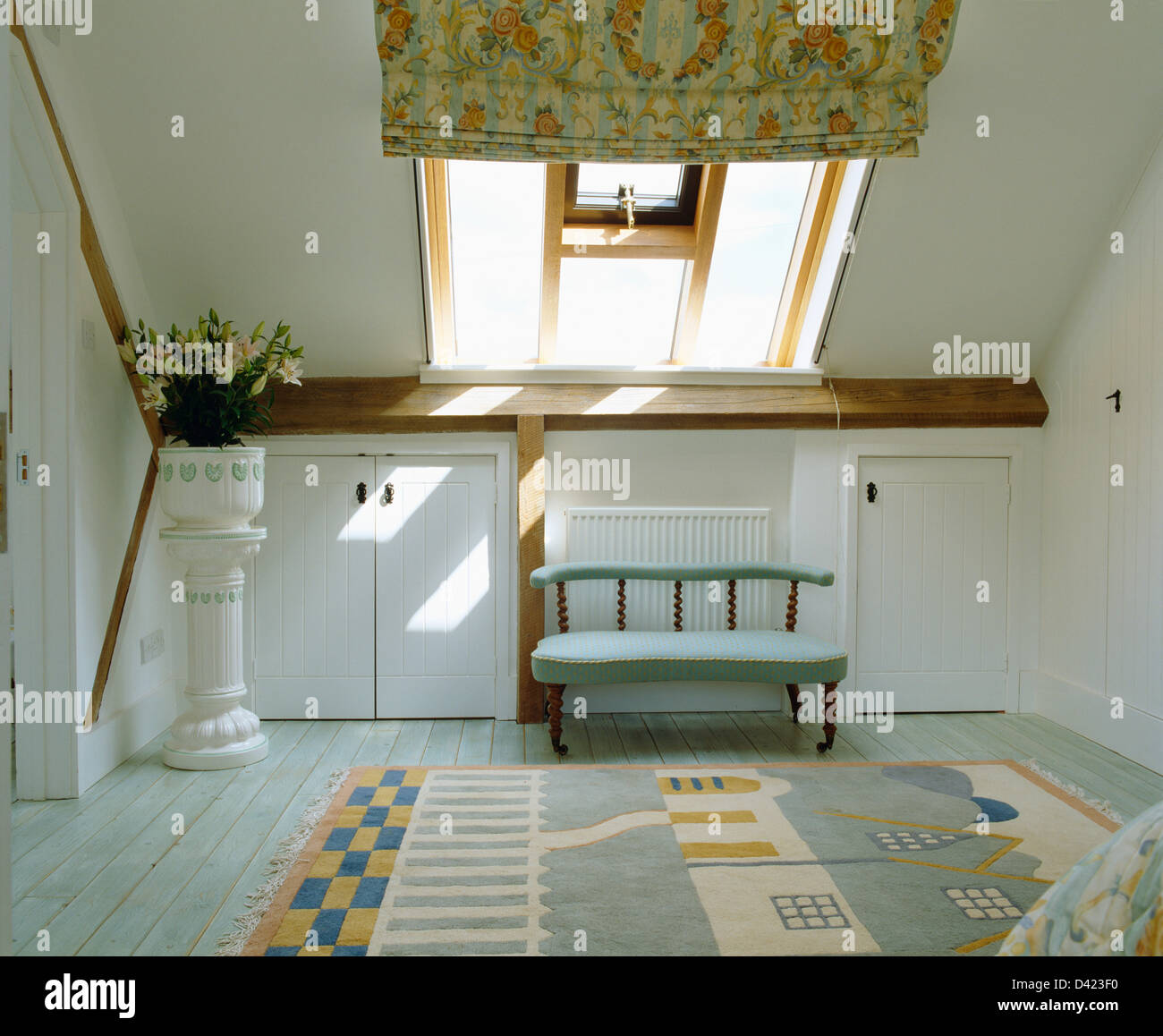 Small blue sofa below Velux window with patterned blind in loft bedroom