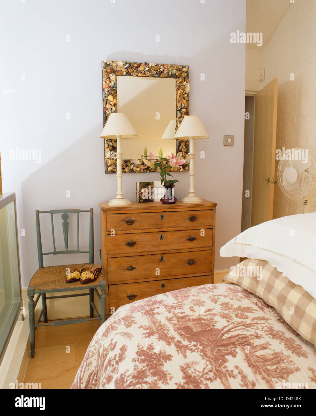 Floral Mirror Above Pine Chest Of Drawers With White Lamps In