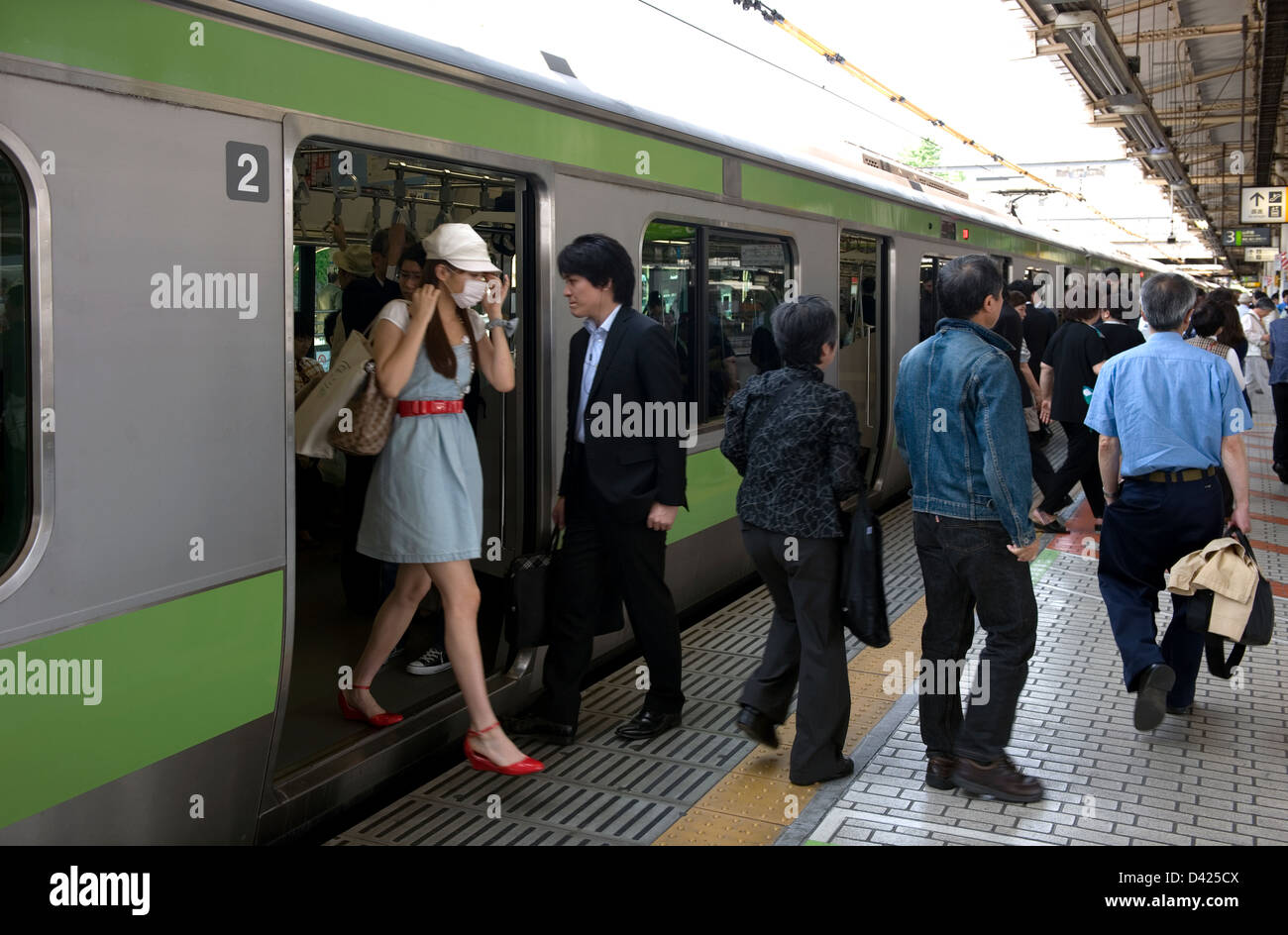 Commuters getting on and off the green Yamanote Loop Line train at the Ueno Station platform in Tokyo. Stock Photo