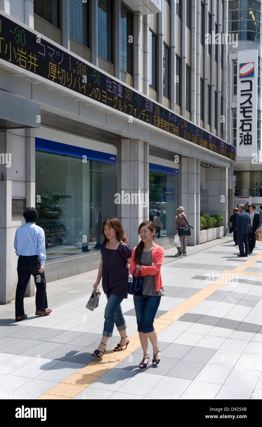 Businessmen and pedestrians walking past electronic stock market ticker tape at  securities firm in downtown Tokyo, Japan. Stock Photo