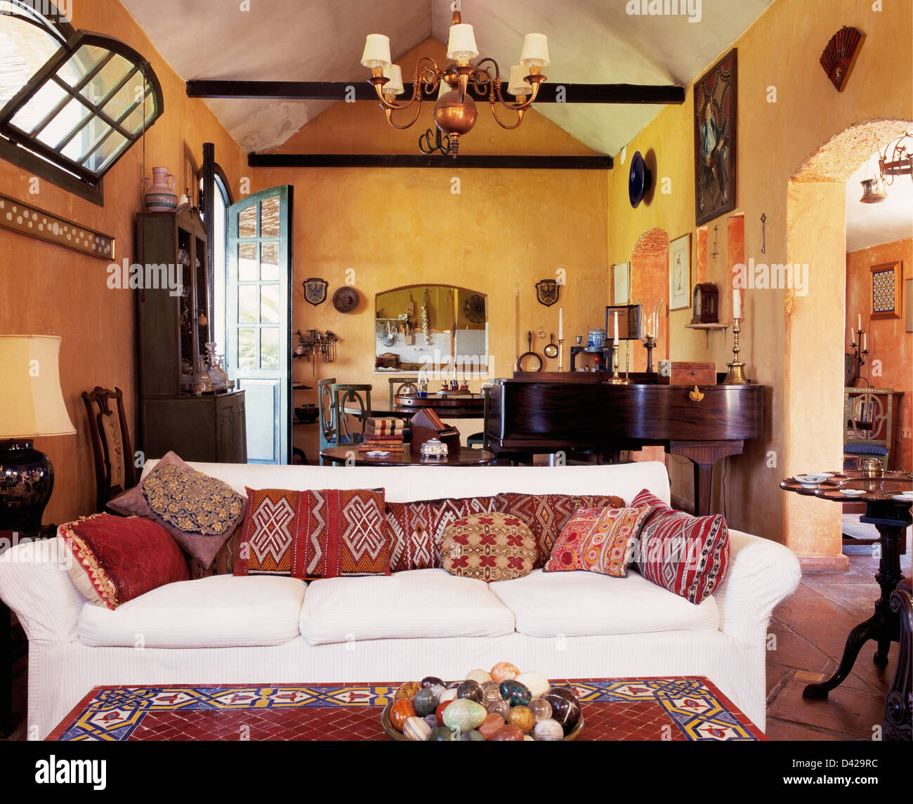 White sofa with patterned cushions in yellow Spanish living room with apex ceiling Stock Photo