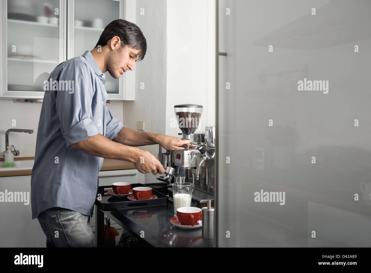 A guy busy making coffee in the kitchen. fridge door on the right is provided as copy space