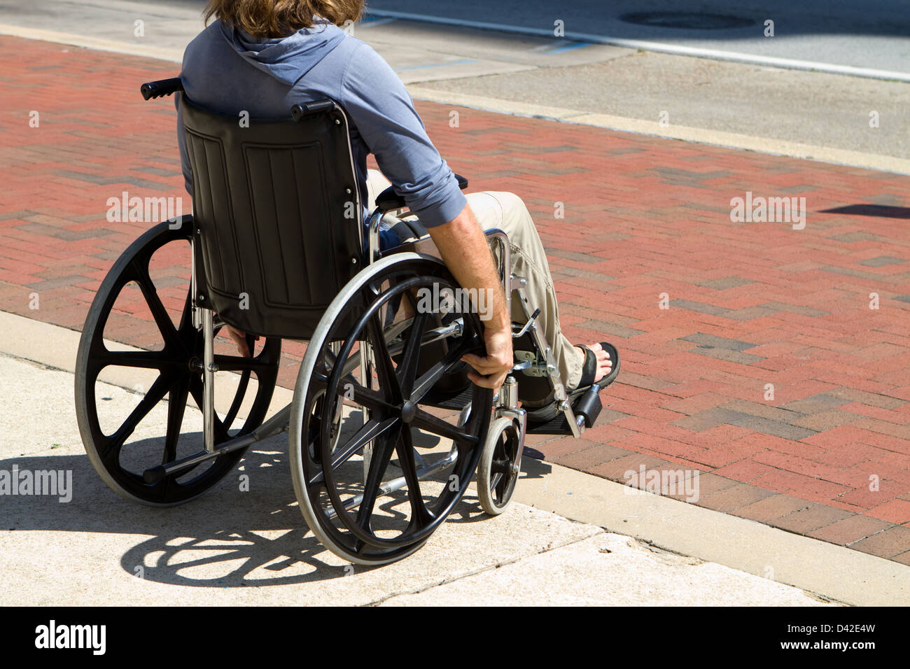 Injured male veteran sitting in his wheelchair rolls on the sidewalk. Stock Photo
