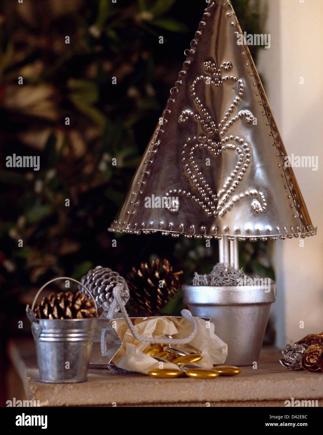 Close-up of hand-made punched tin Christmas tree in silver painted pot on table with miniature zinc buckets with pine cones Stock Photo