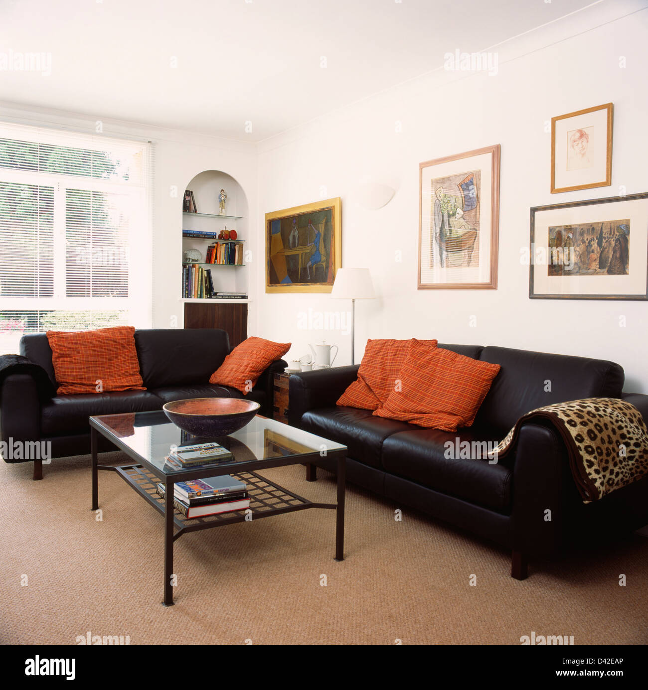 Orange cushions on black leather sofas in living room with beige carpet and  glass-topped coffee table Stock Photo - Alamy