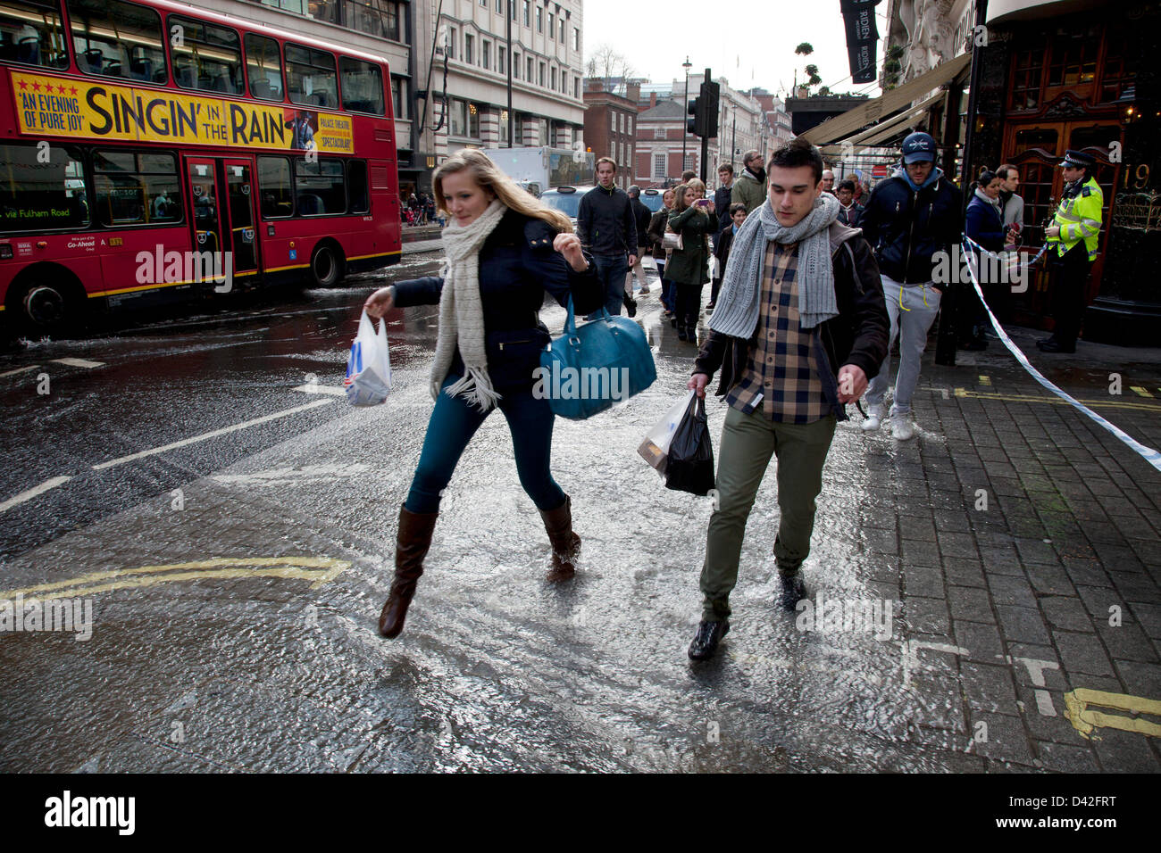 London, UK. Saturday 2nd March 2013. Burst water main causes flooding disruption in central London. People run through the flowing water. Stock Photo
