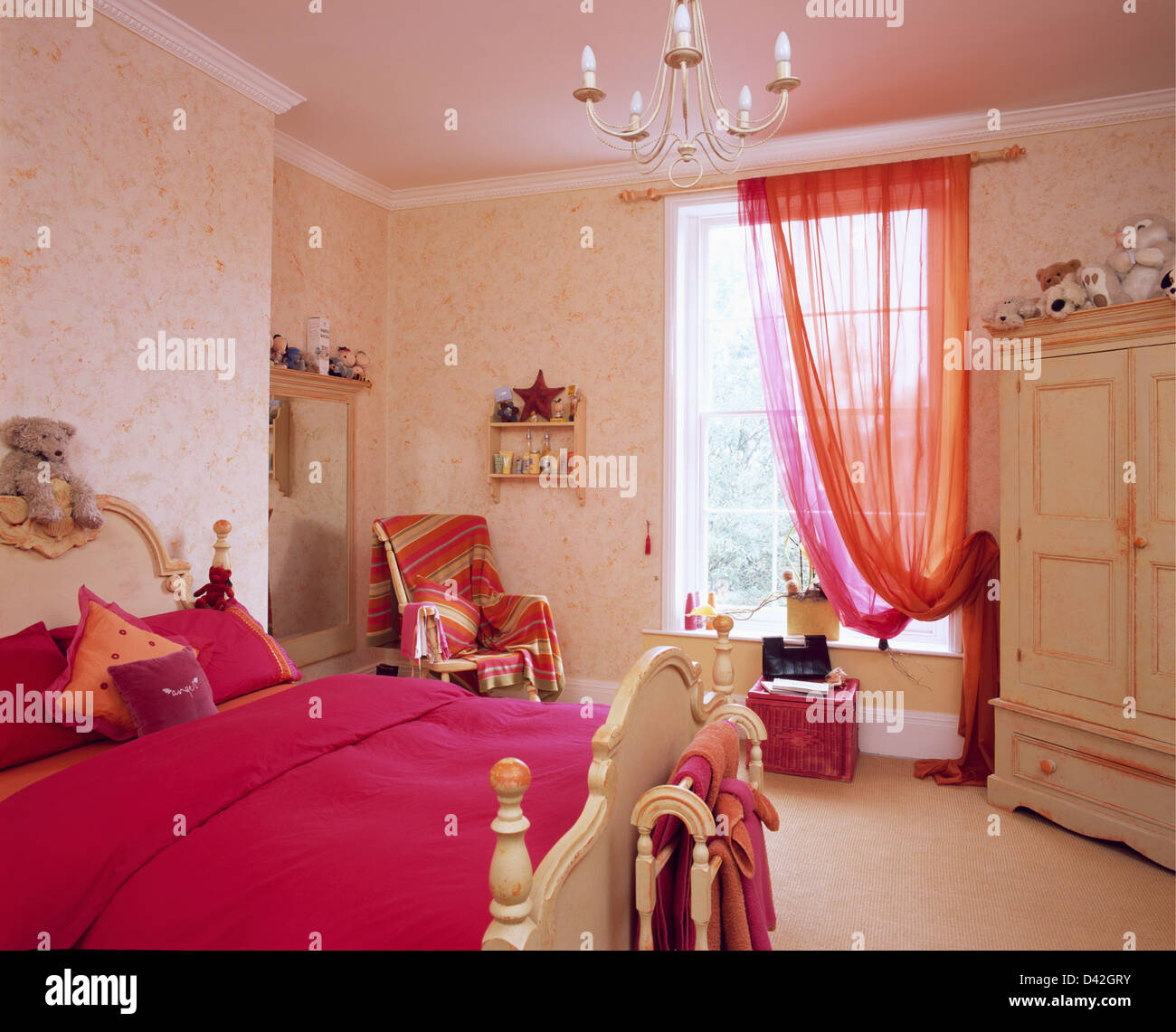 Bright pink bed cover on bed in teenage bedroom with pink voile curtain