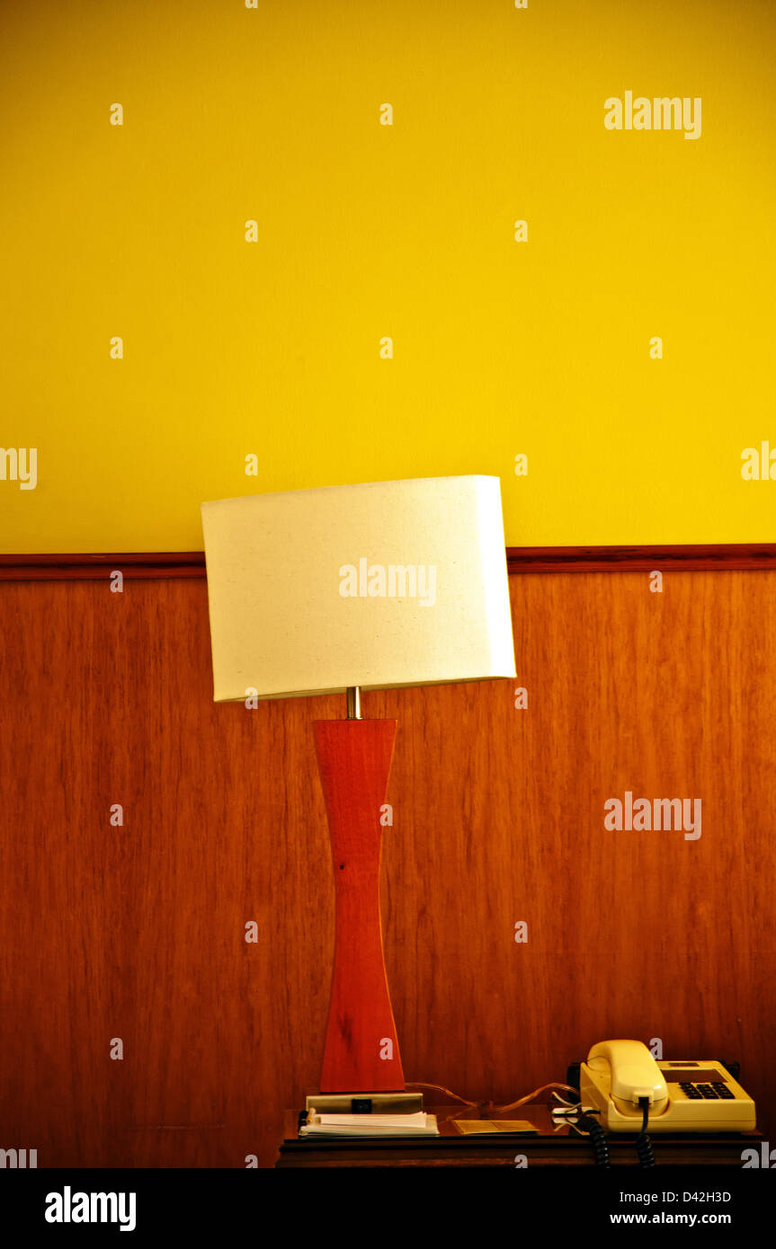 A lamp and telephone on a desk with a yellow and wood wall. Stock Photo