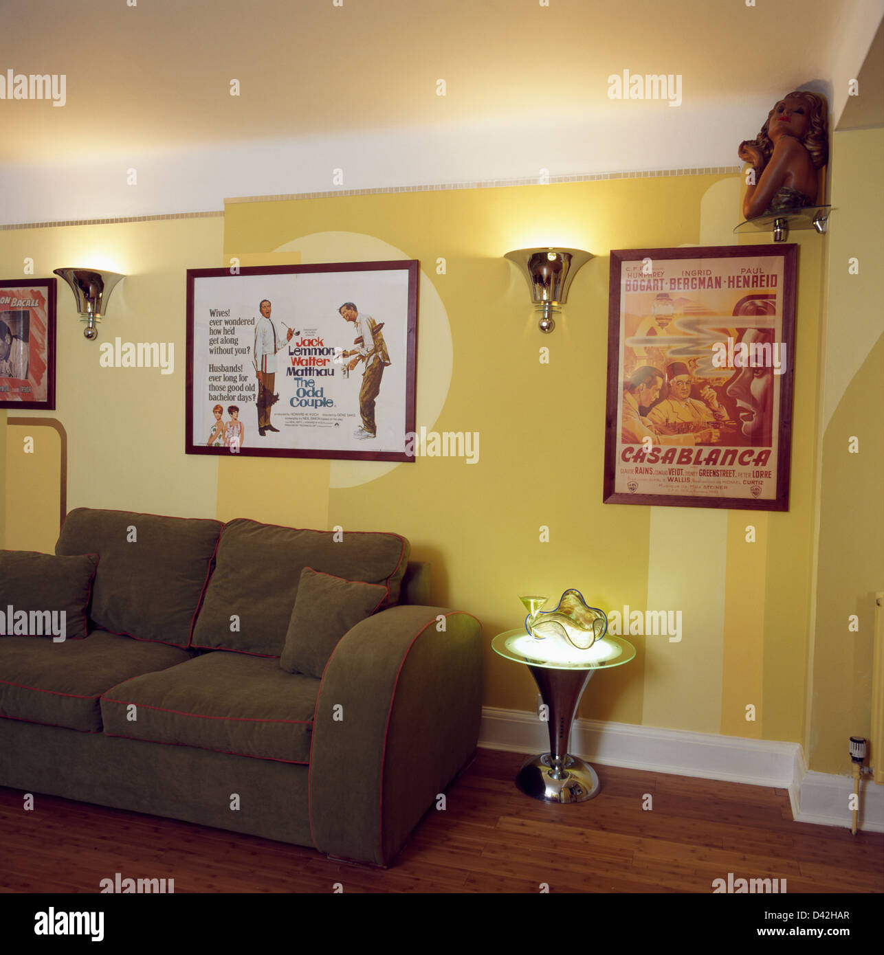 Brown sofa and small chrome table in retro living room with Forties film posters on the wall and painted yellow wall decoration Stock Photo