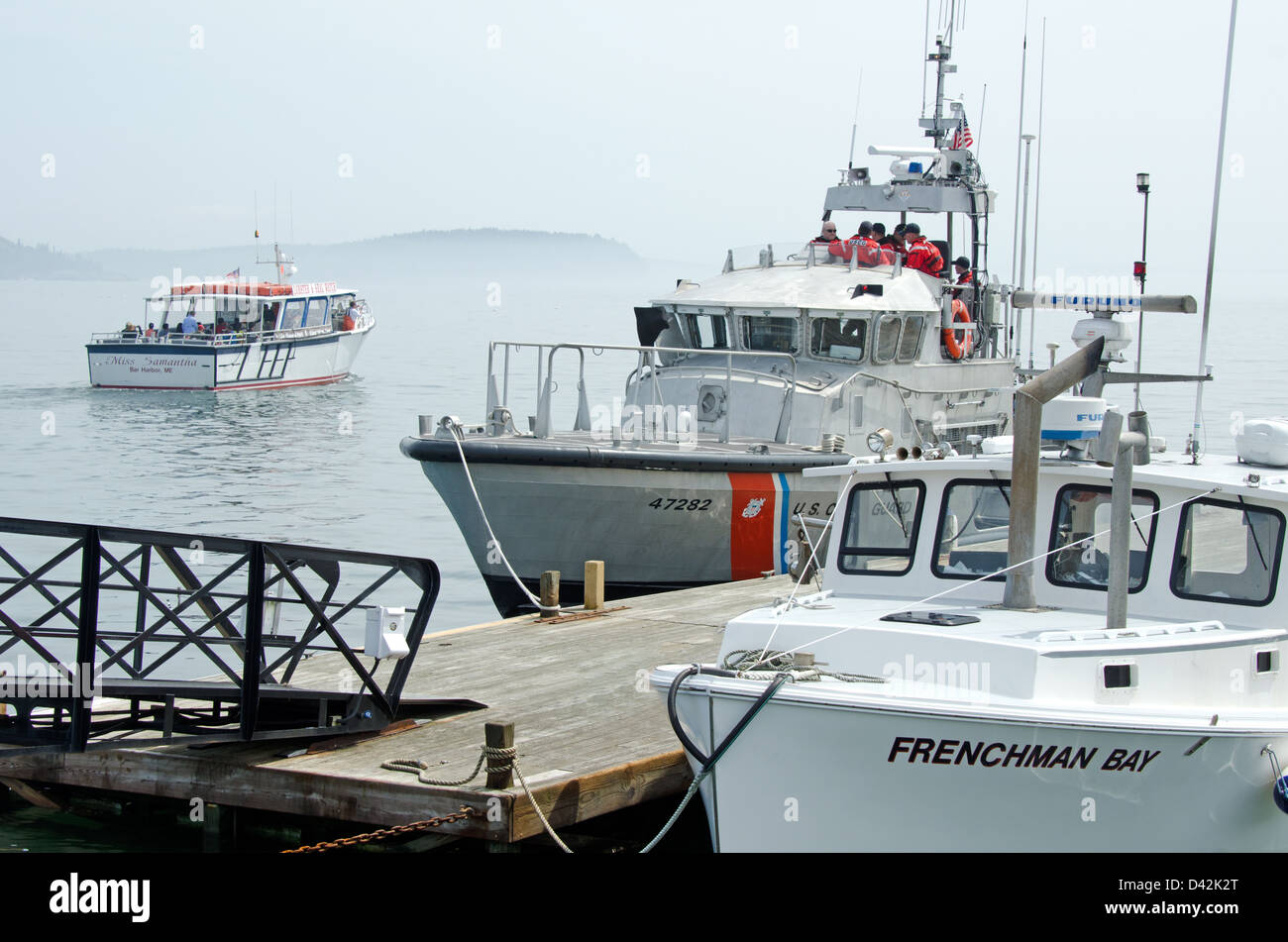 A tour boat, a Coast Guard patrol boat, and a lobster boat cross paths on a foggy day at the Bar Harbor Town Pier. Stock Photo