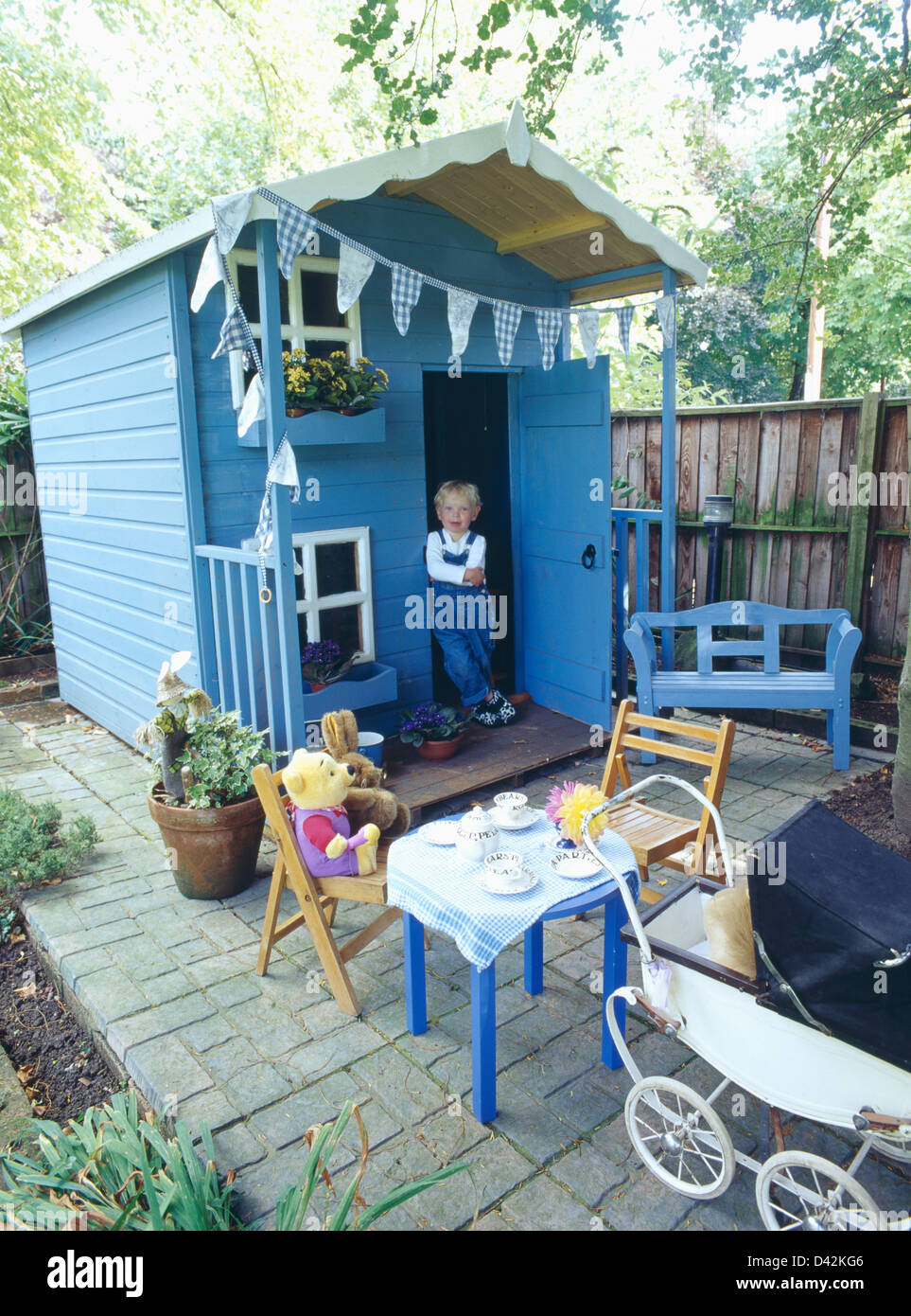 Small Girl Wearing Dungarees Standing In Doorway Of Blue Wooden